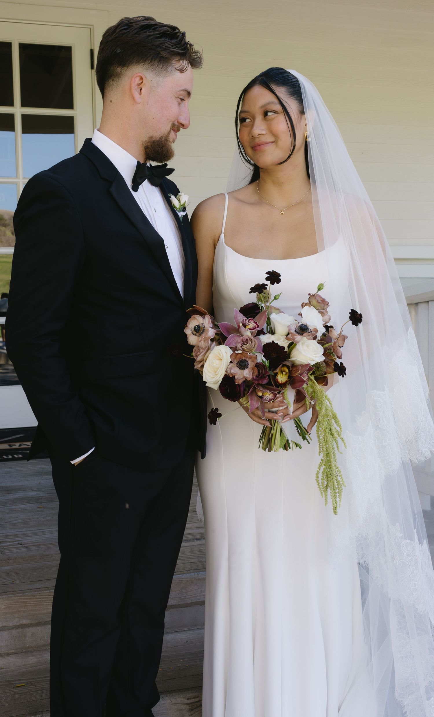 A couple shares an intimate moment on their wedding day, with the bride in white and groom in a black tuxedo.