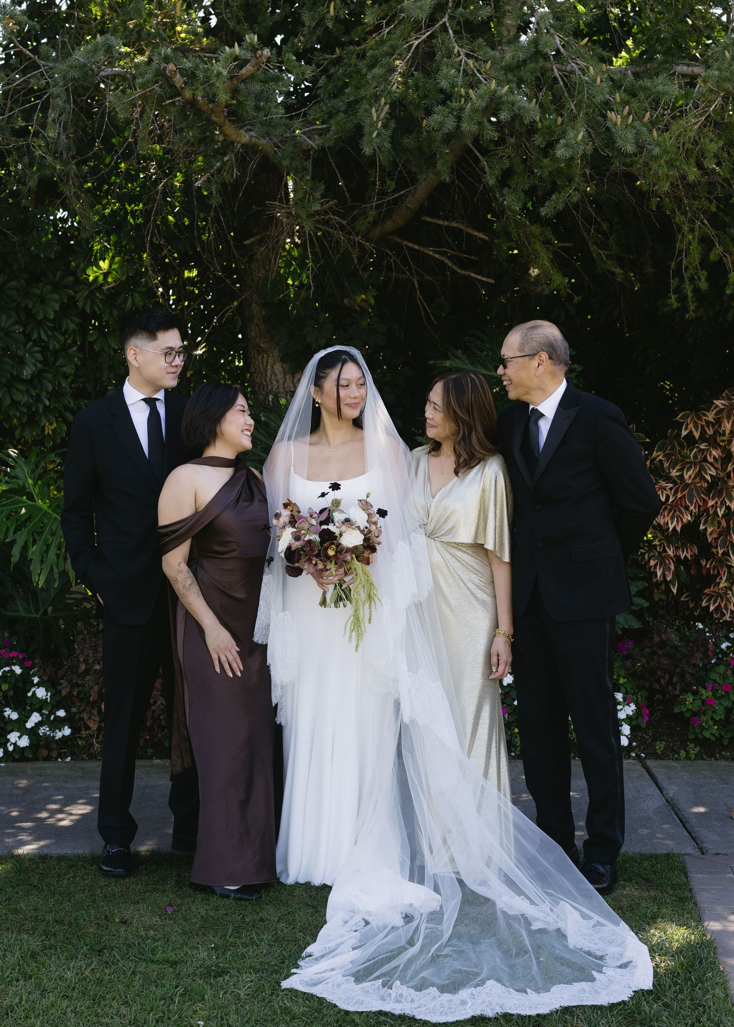 Wedding party poses outdoors in formal attire with bridesmaids in brown dresses and flowing white bridal gowns.