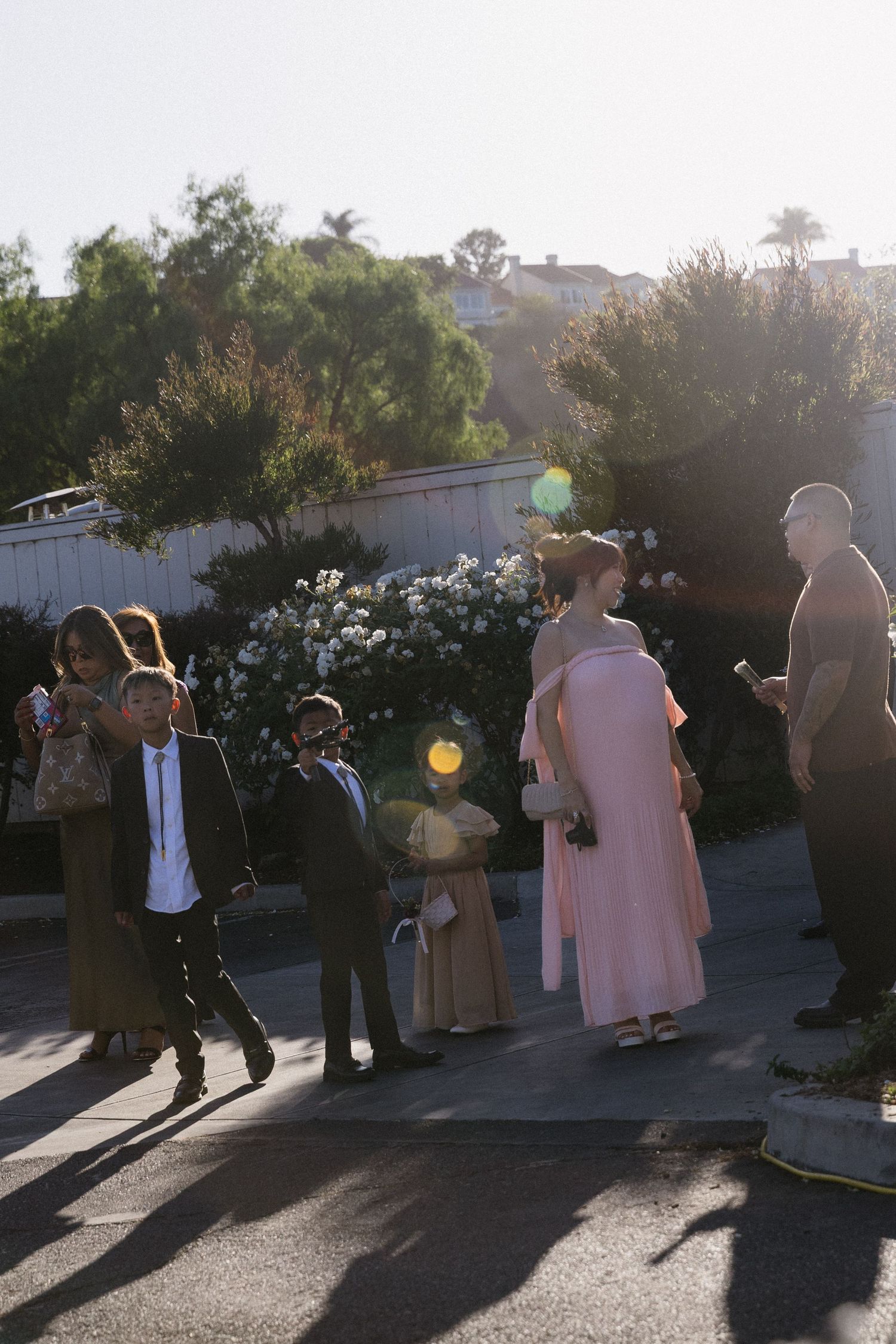 Wedding party silhouettes against sunset creating dramatic shadows on pavement.