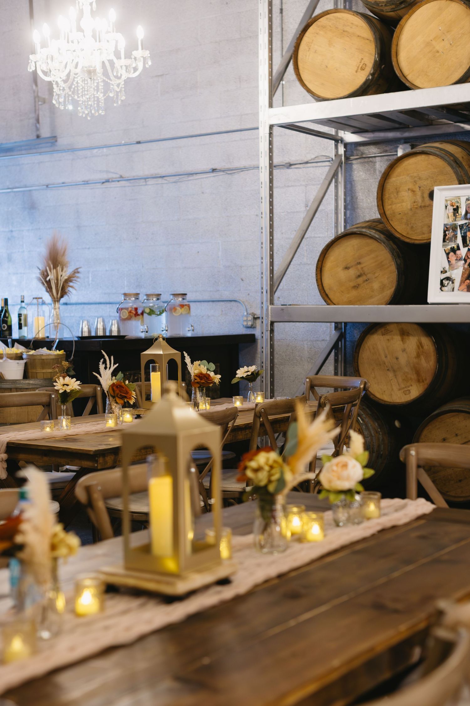 Rustic wooden table decorated with candles and floral centerpieces in a wine barrel room with chandeliers.