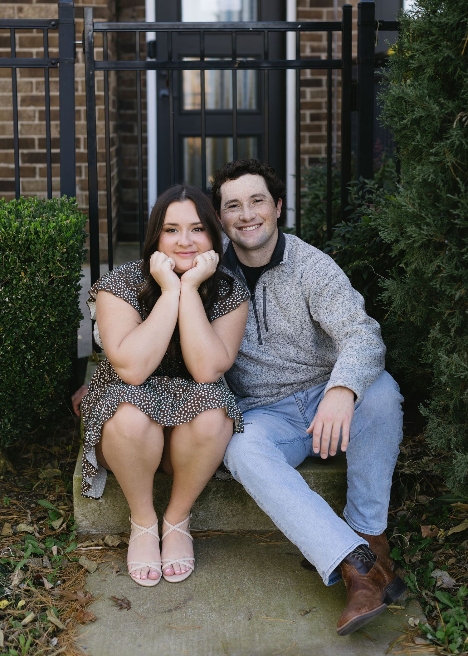 A couple sits casually together on concrete steps in front of a brick building.