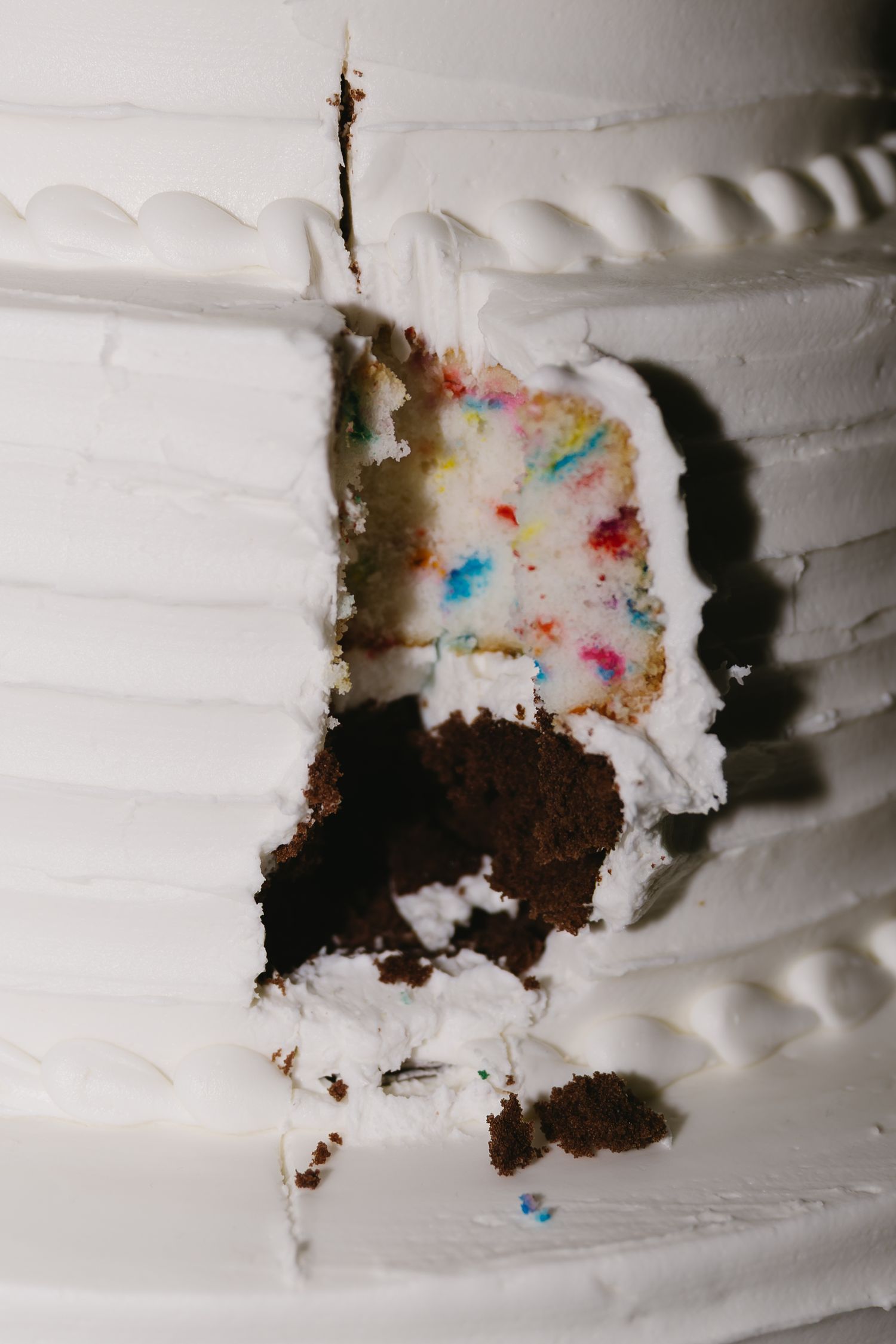 Close-up of a sliced wedding cake showing layers of colorful confetti sprinkles and white frosting.