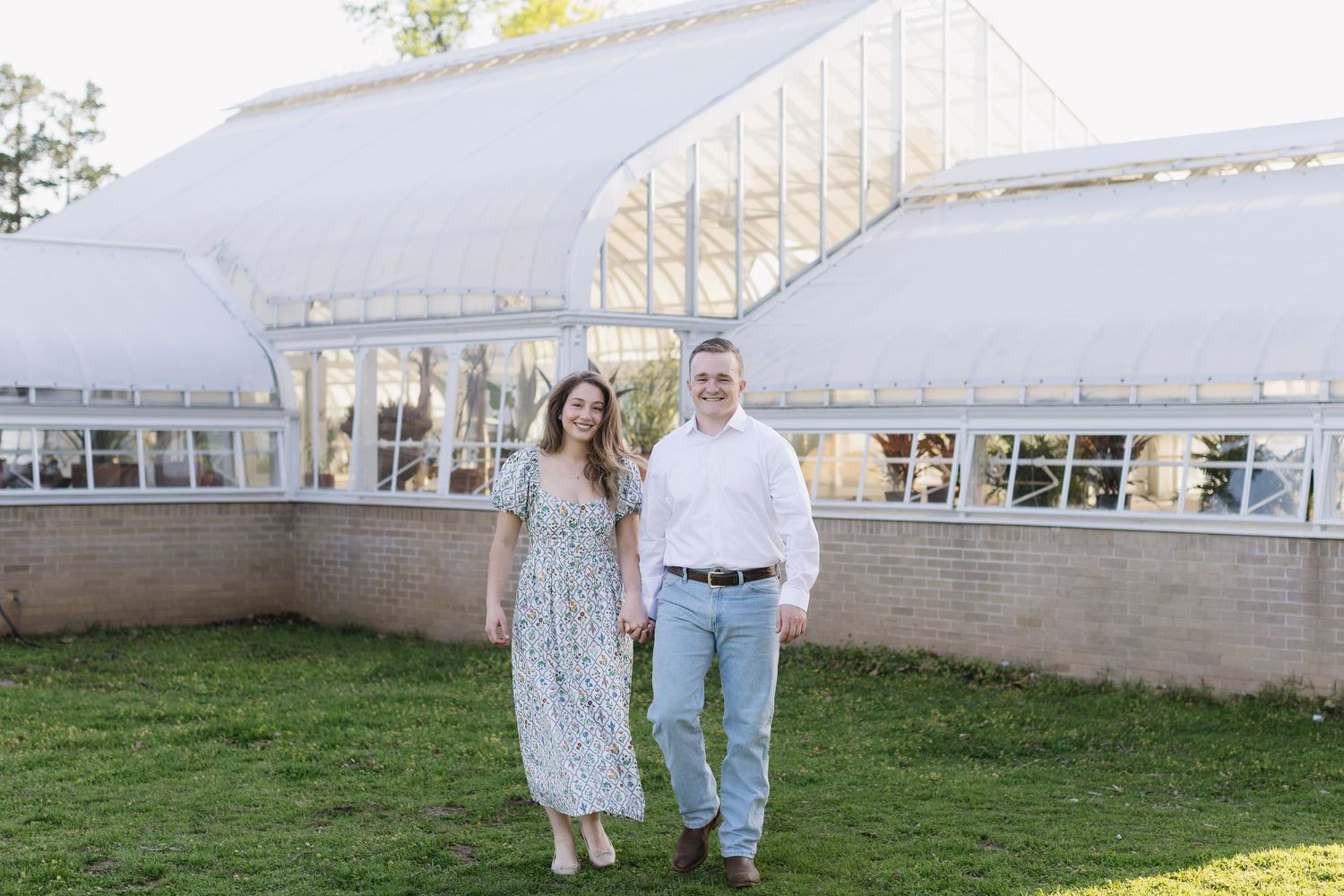 A romantic couple embraces near a greenhouse in casual spring outfits.