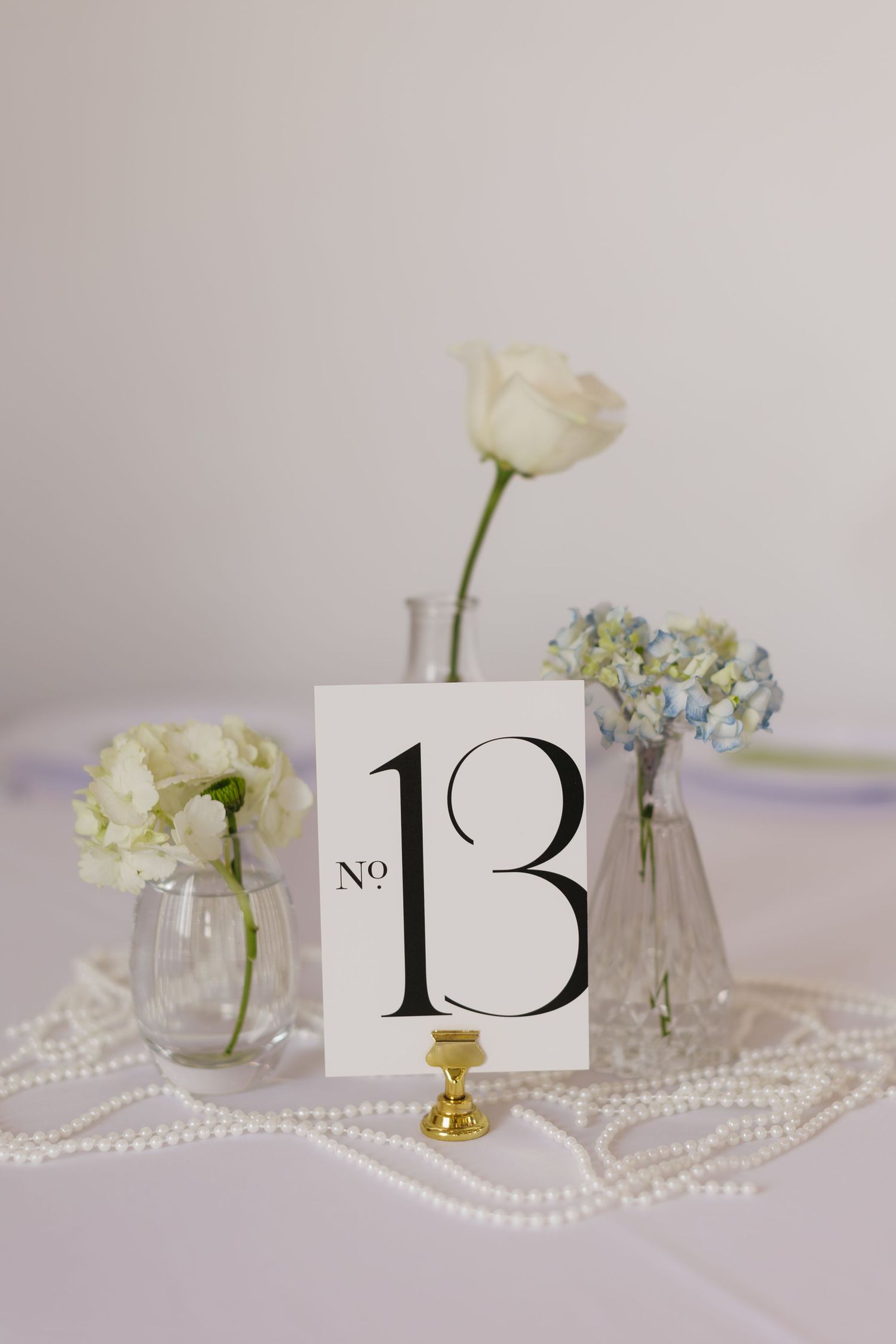 Elegant table settings with white flowers, pearl strands and table number 13 in classic typography.