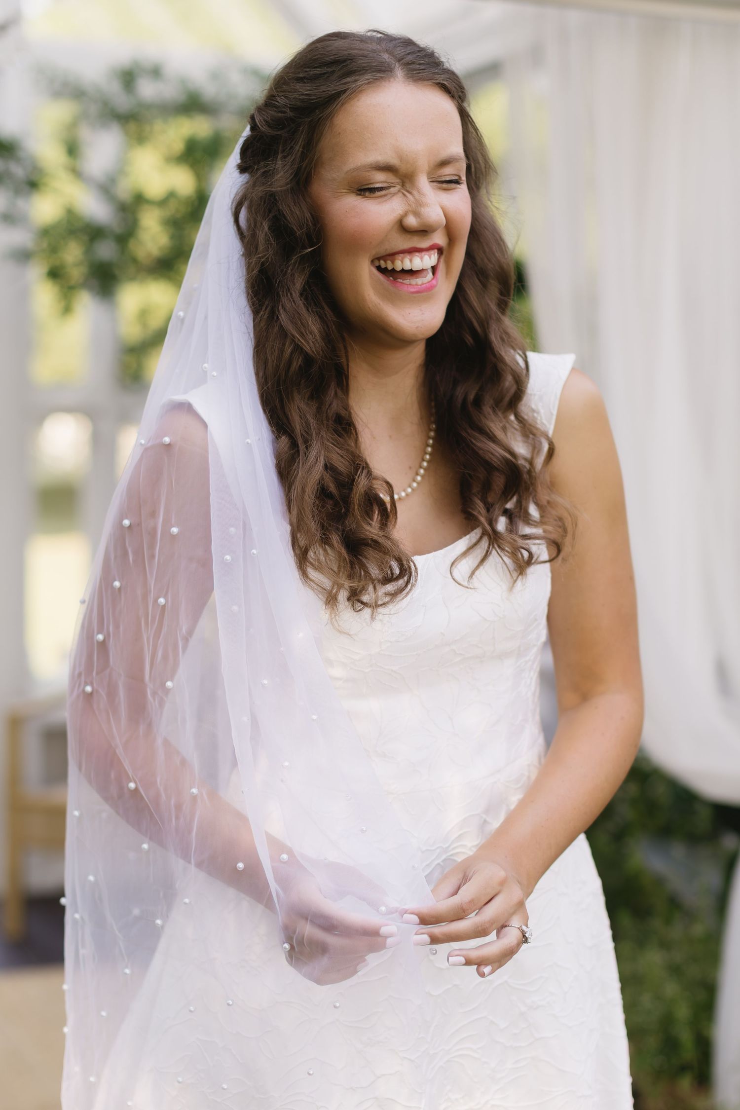 A joyful bride in a white wedding dress and veil laughs while posing for bridal portraits.