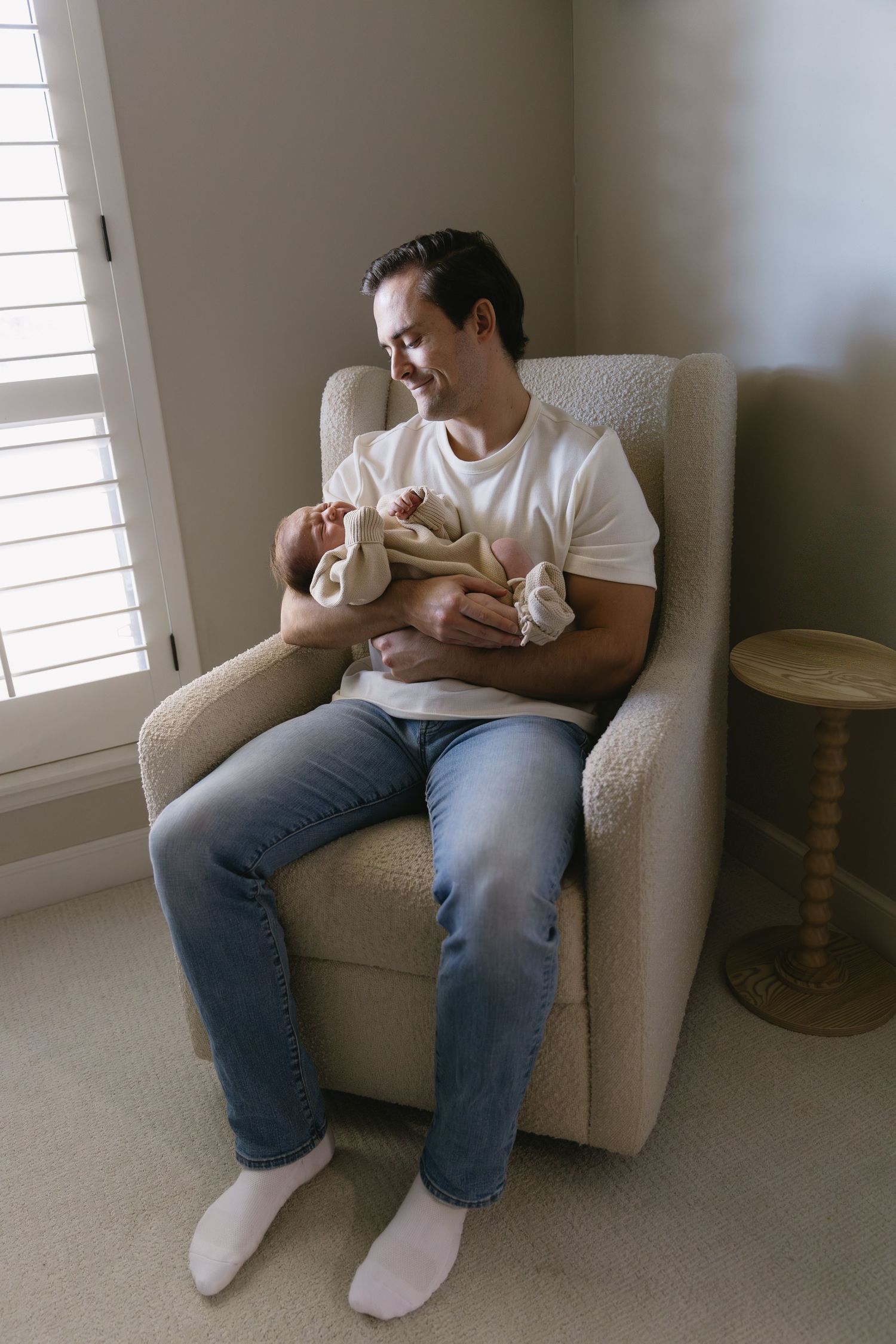 Casual home scene showing people relaxing in a beige armchair near a window.