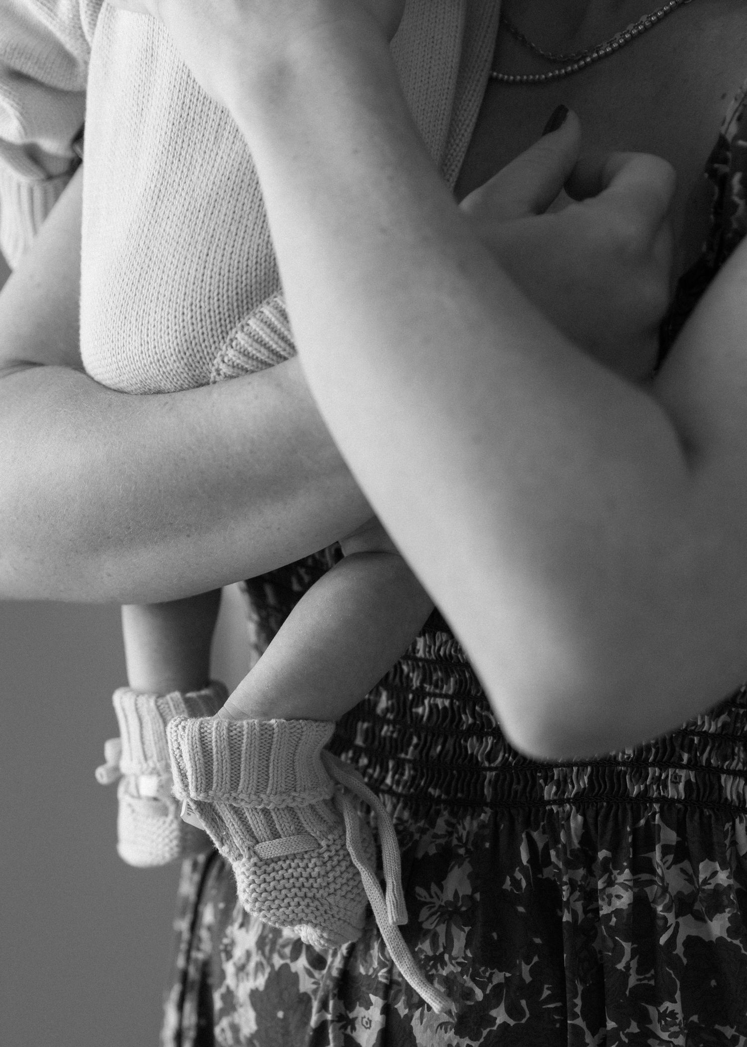 Black and white detail shot of arms holding a baby wearing a white knitted sweater.
