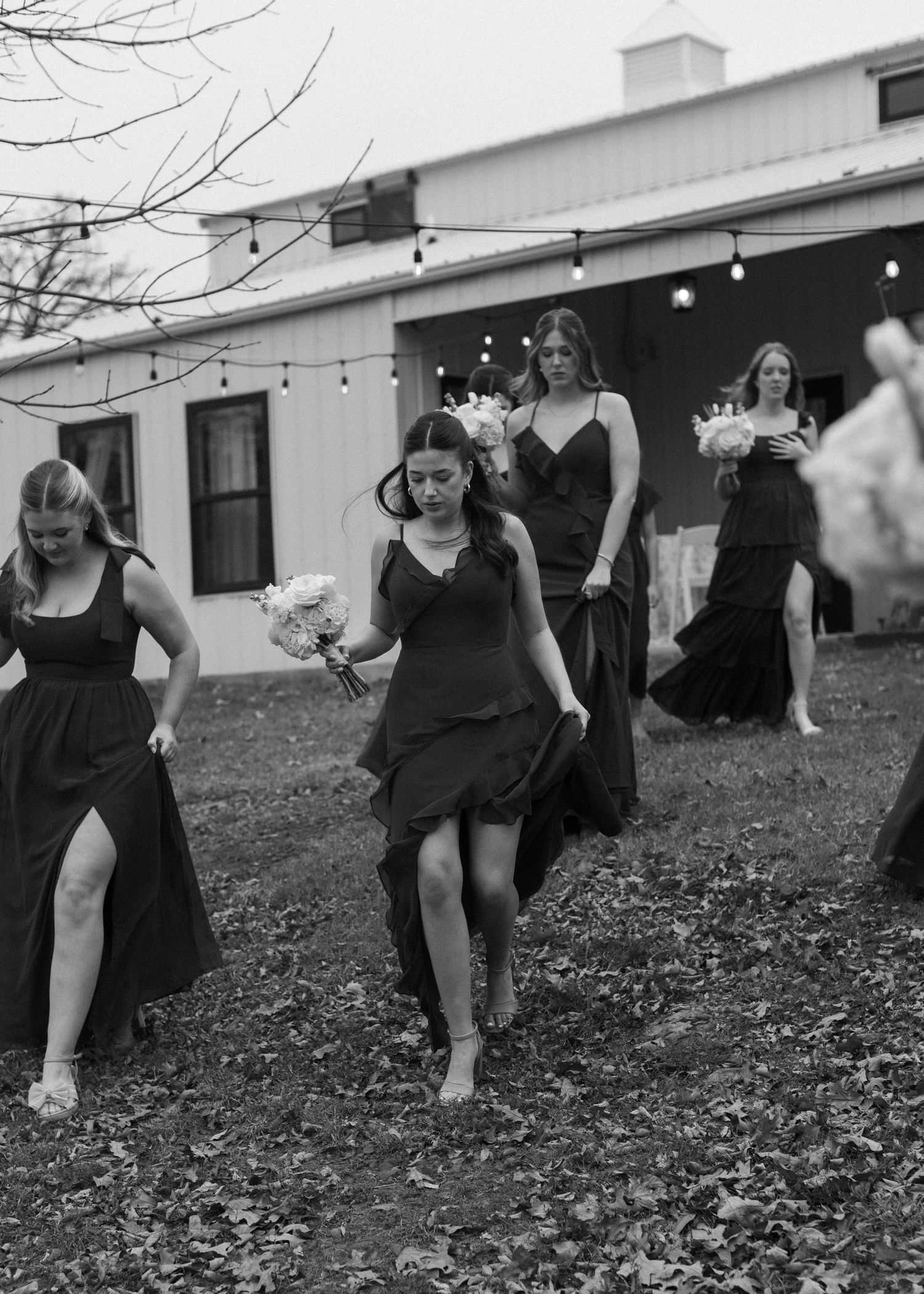 Wedding party members in black dresses perform synchronized dance moves on fallen leaves.