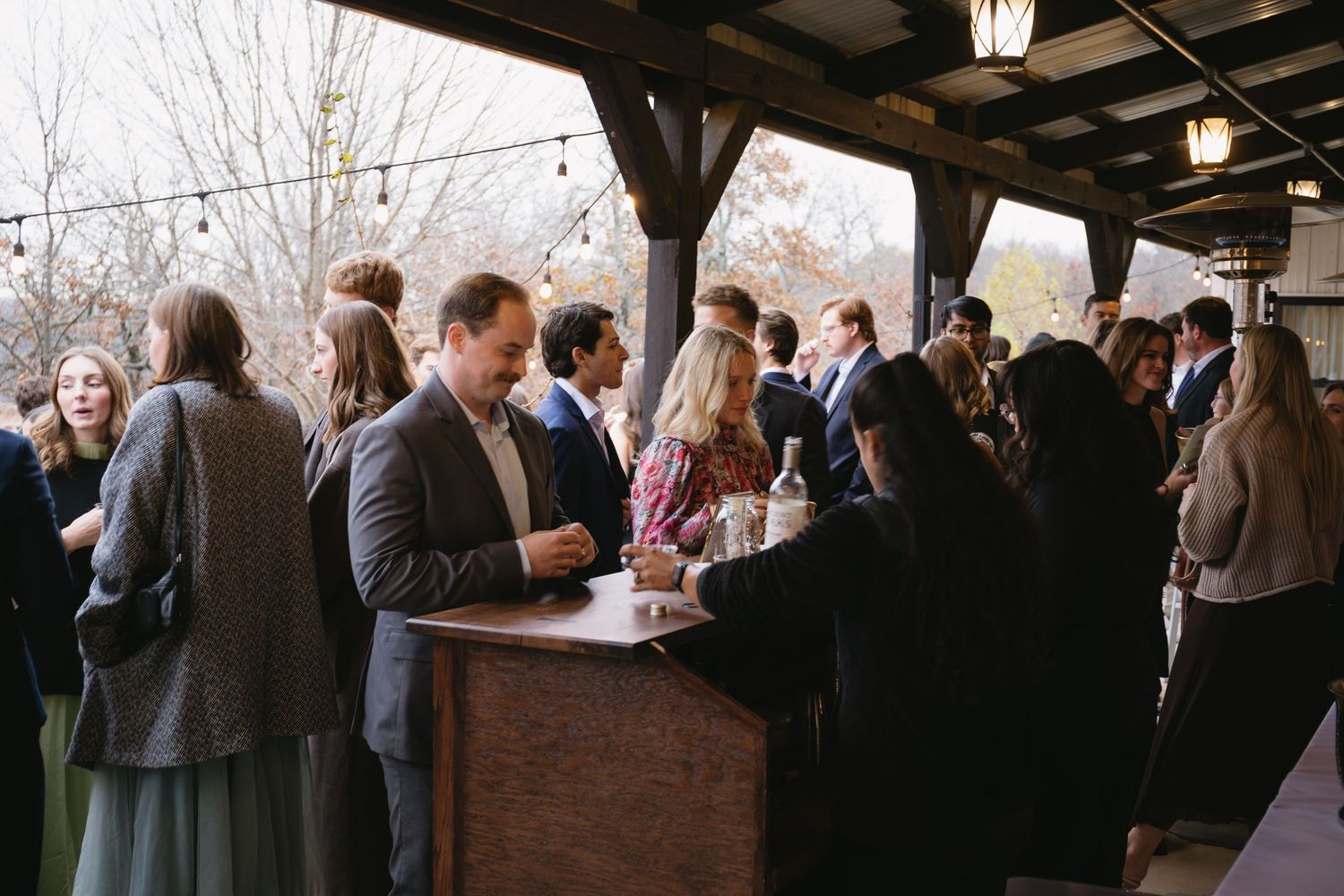 Large group of wedding guests mingling on an outdoor covered patio during a reception.