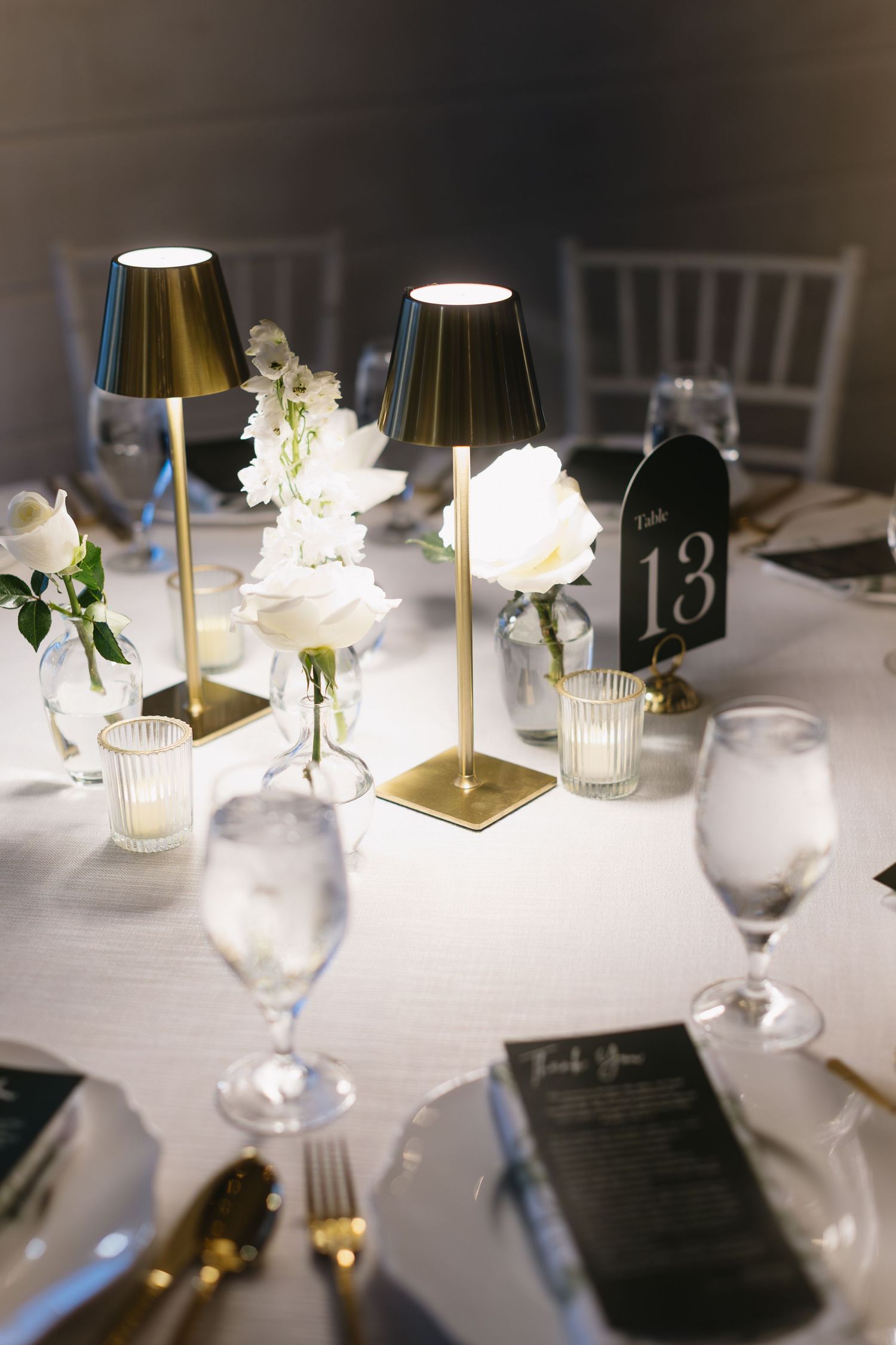 Elegant wedding table setting with gold lamps, white roses, and table number 13.