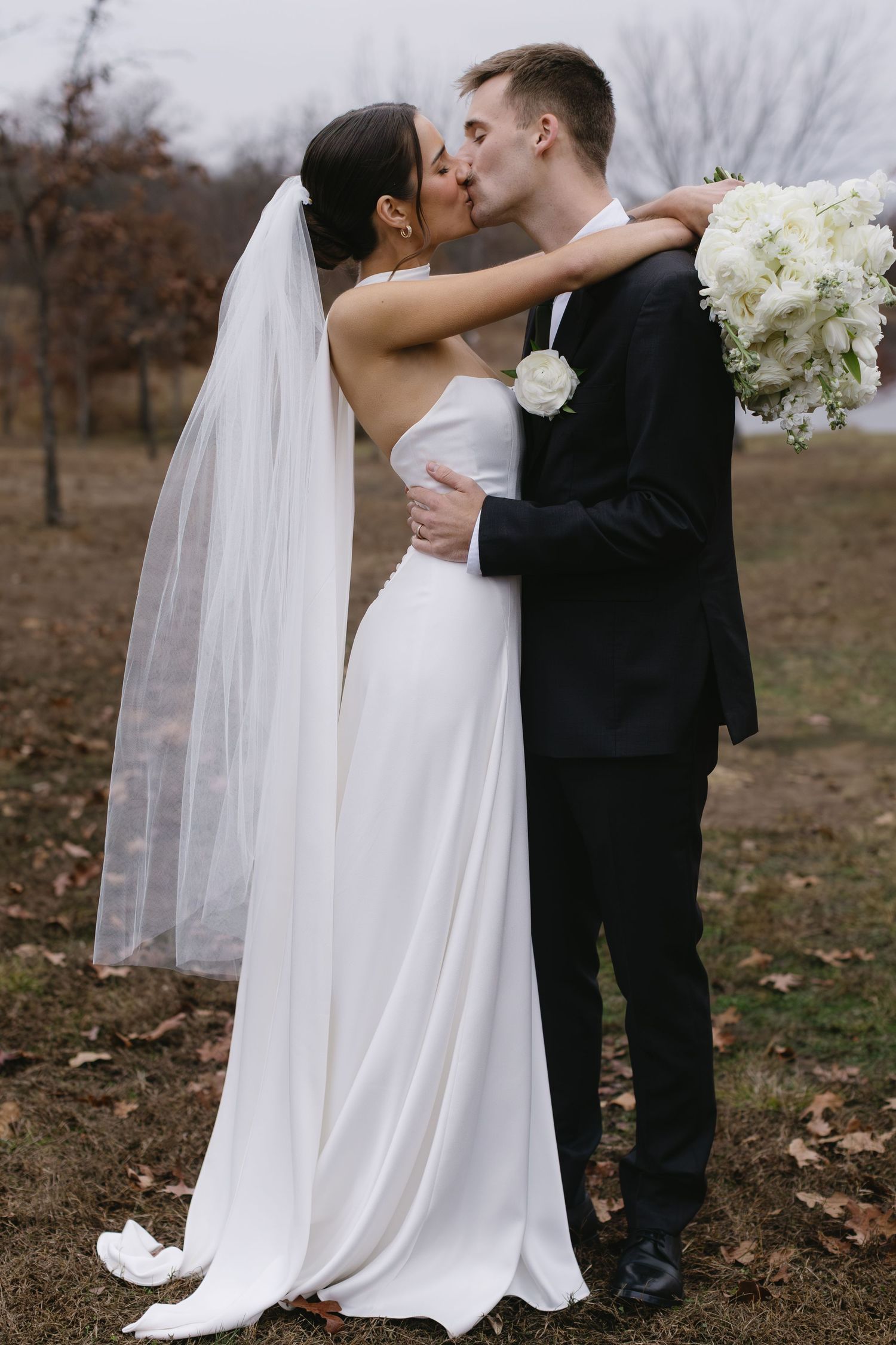 Elegant wedding couple shares intimate moments in a fall setting with white flowers and long veil.