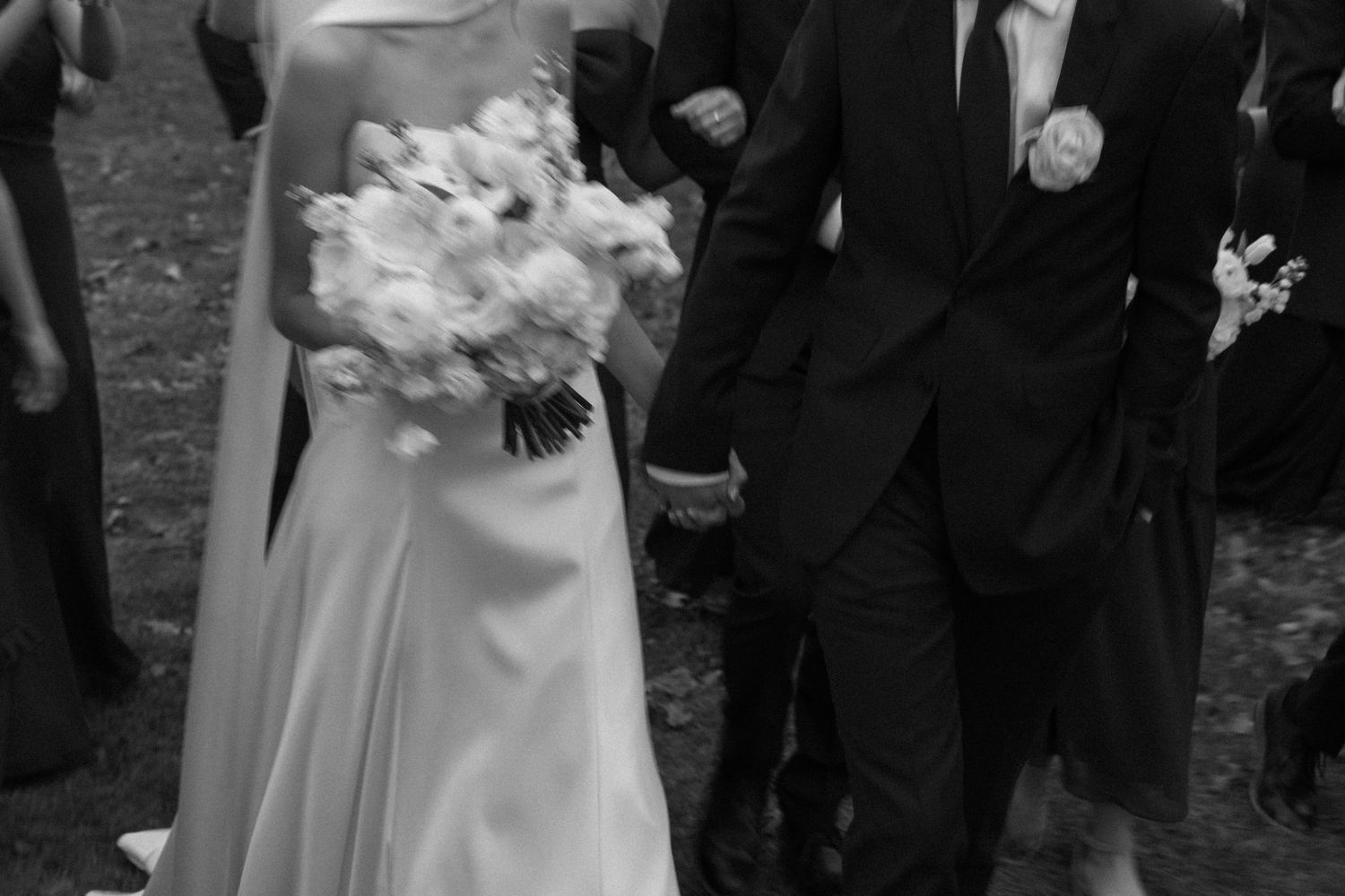 Wedding party members in formal attire stand together holding white floral bouquets.