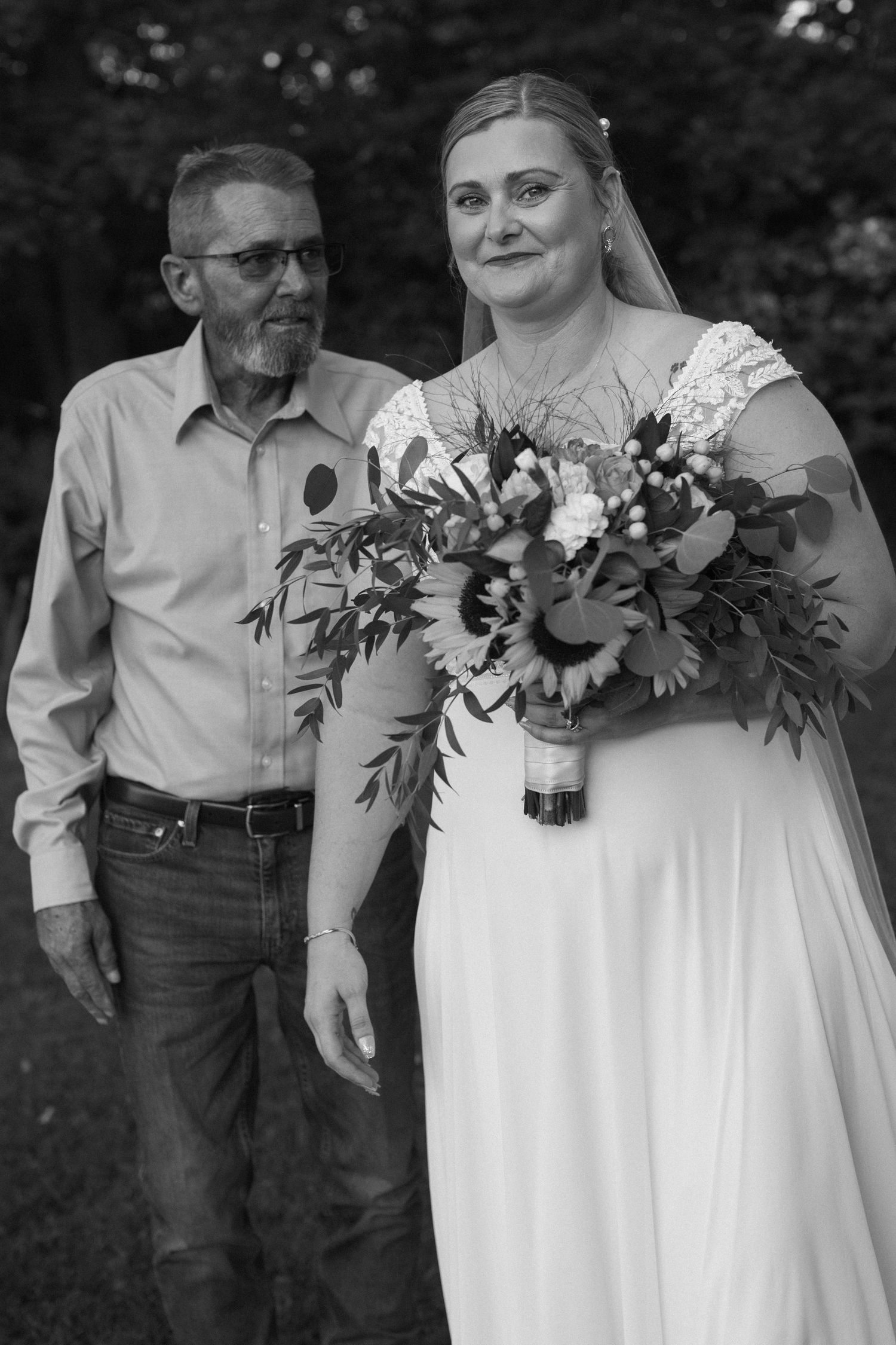 A bride in a white dress holds a colorful floral bouquet during an outdoor wedding ceremony.