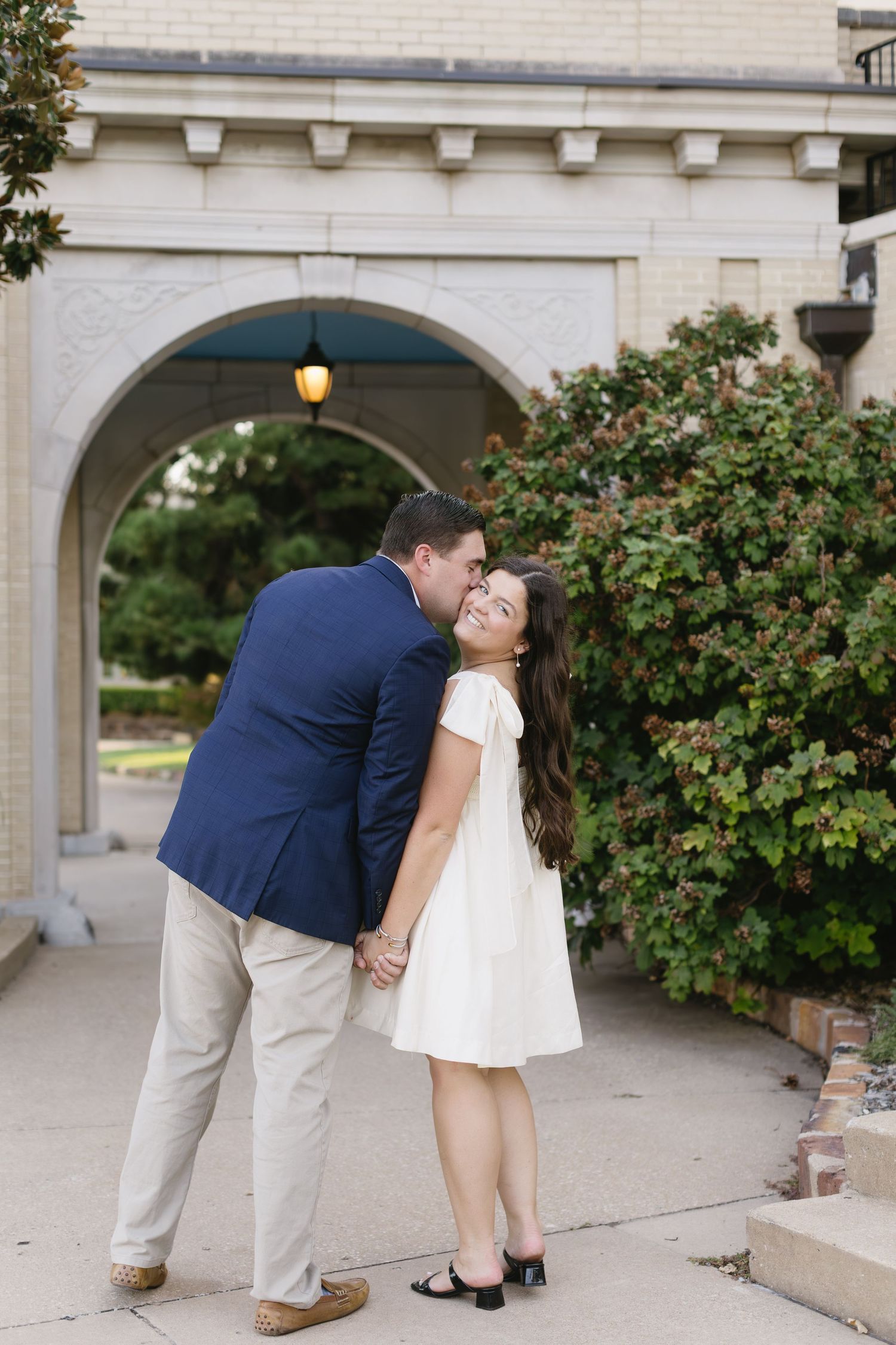 A couple shares romantic moments under an ornate stone archway with hanging lamps.