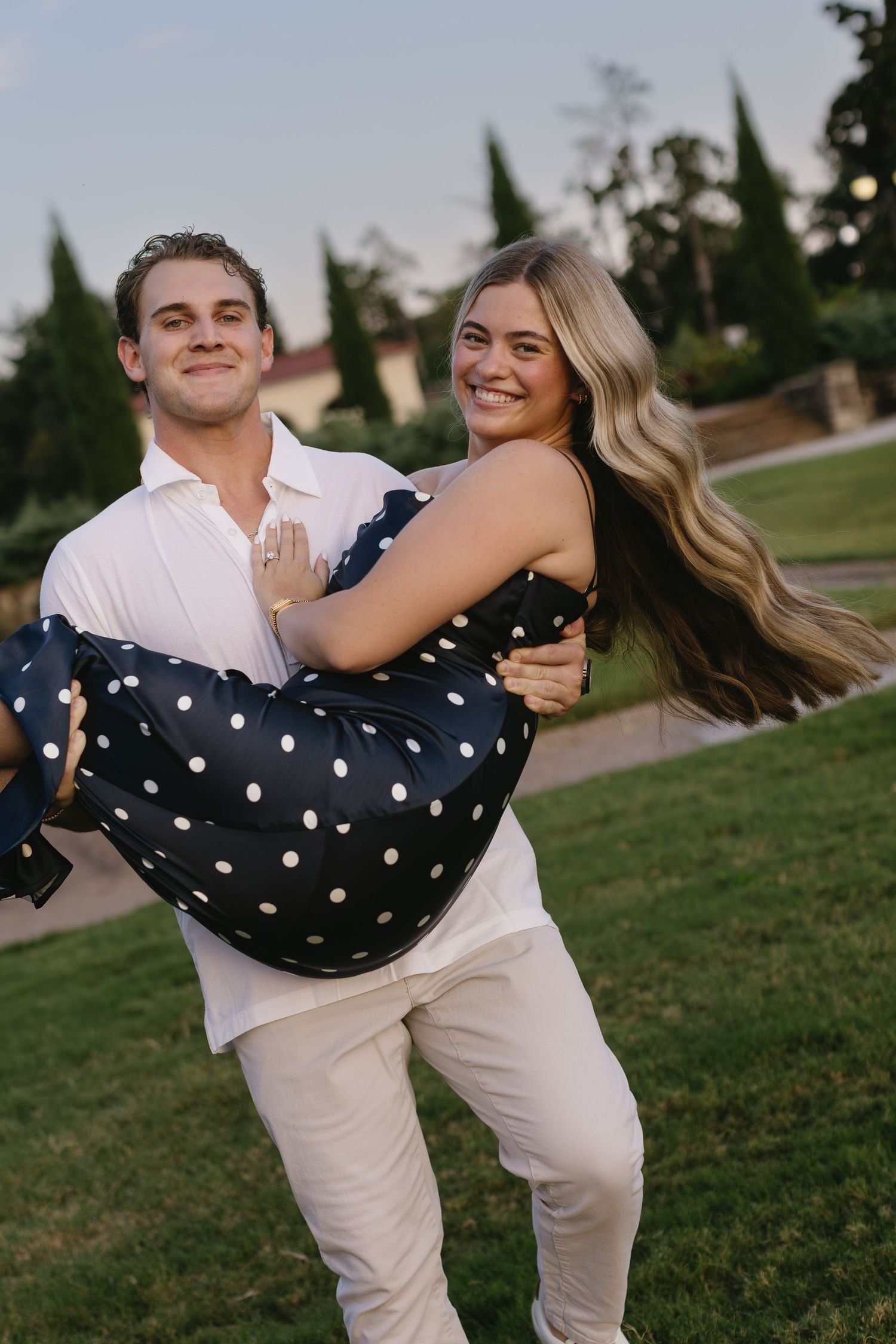 Playful lift pose outdoors with polka dot dress and white outfit coordination.