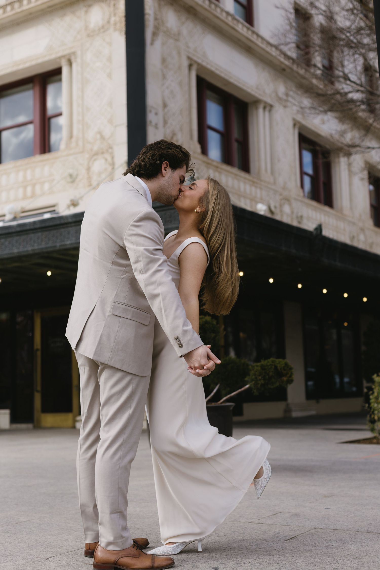 A romantic dip pose between a couple in coordinating beige and white formal wear.