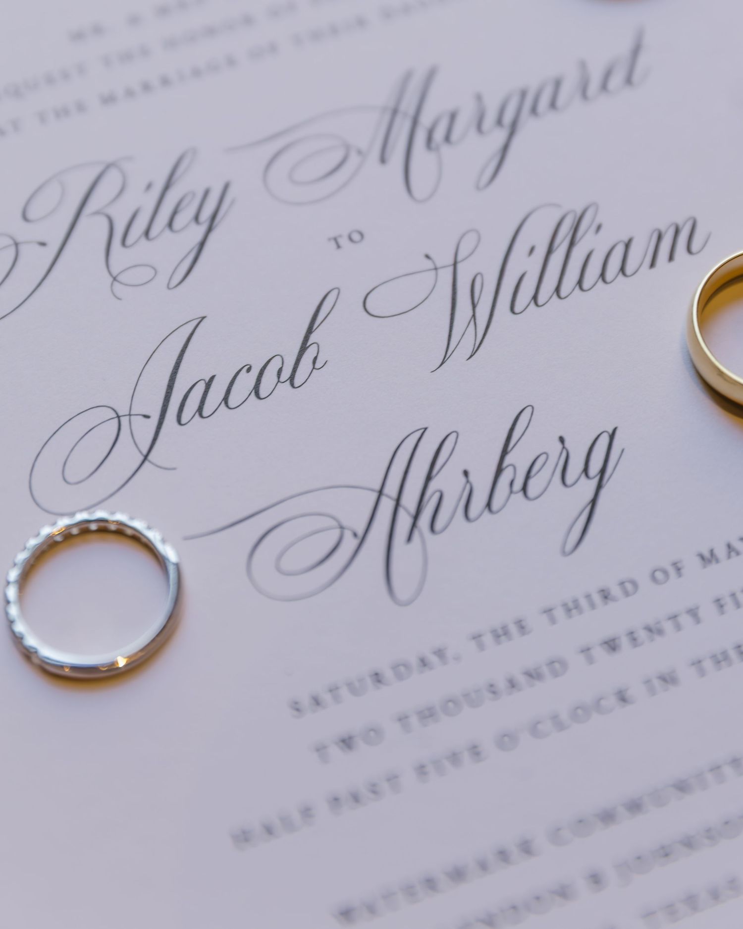 Wedding invitation with elegant calligraphy lettering and wedding rings on white paper in a macro shot.