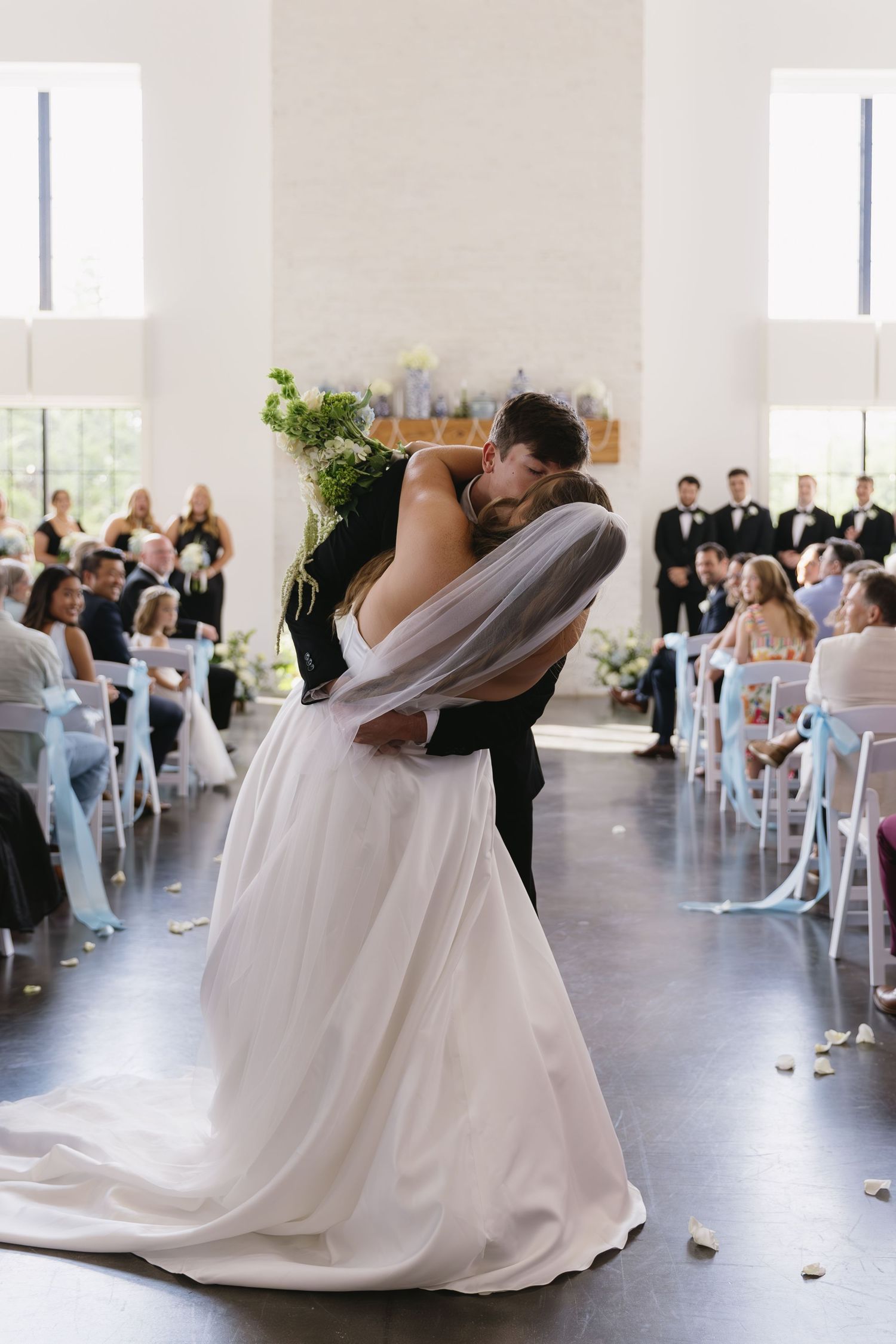 Wedding couple shares their first dance in an airy white reception venue with guests watching.