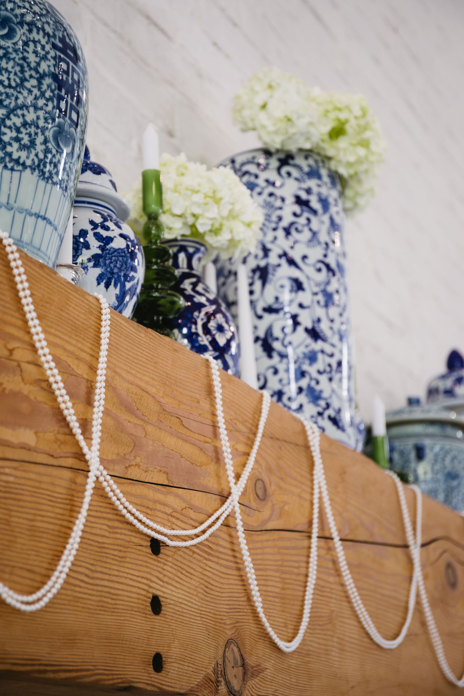 Blue and white porcelain vases with pearl strands displayed on wooden shelf.