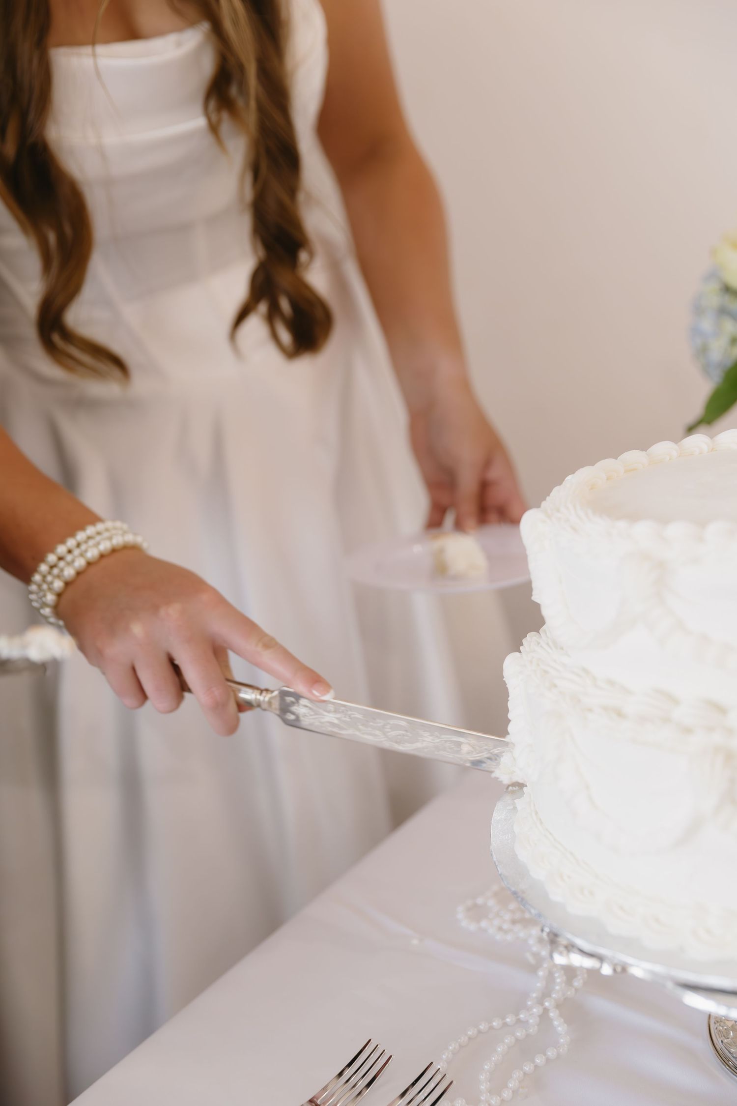 Hands in white serving and cutting a traditional wedding cake with pearls.