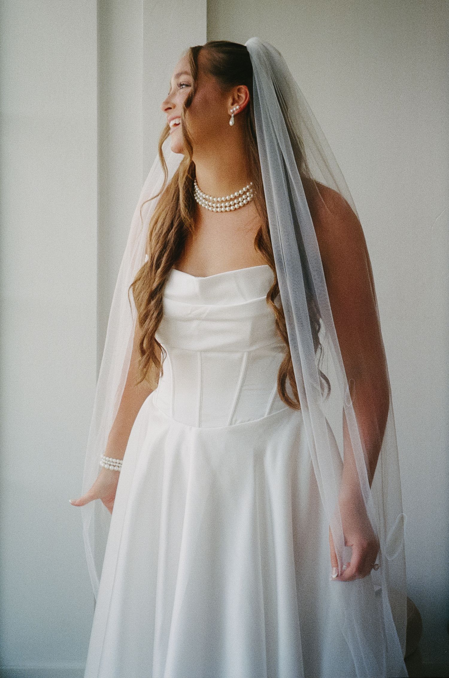Elegant bridal portrait featuring white dress and flowing veil against neutral background.