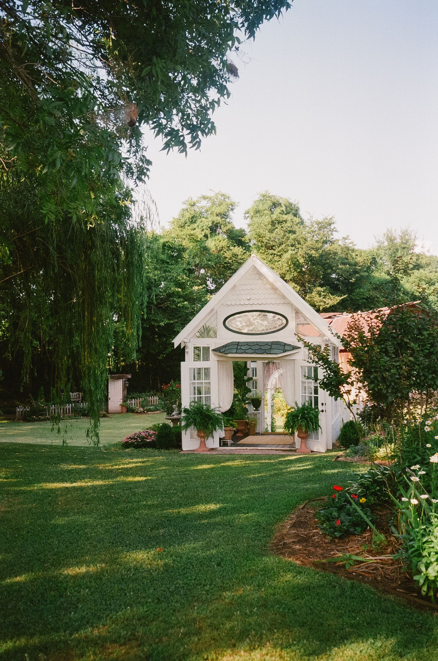 White garden gazebo structures nestled among trees and greenery on a sunny lawn.