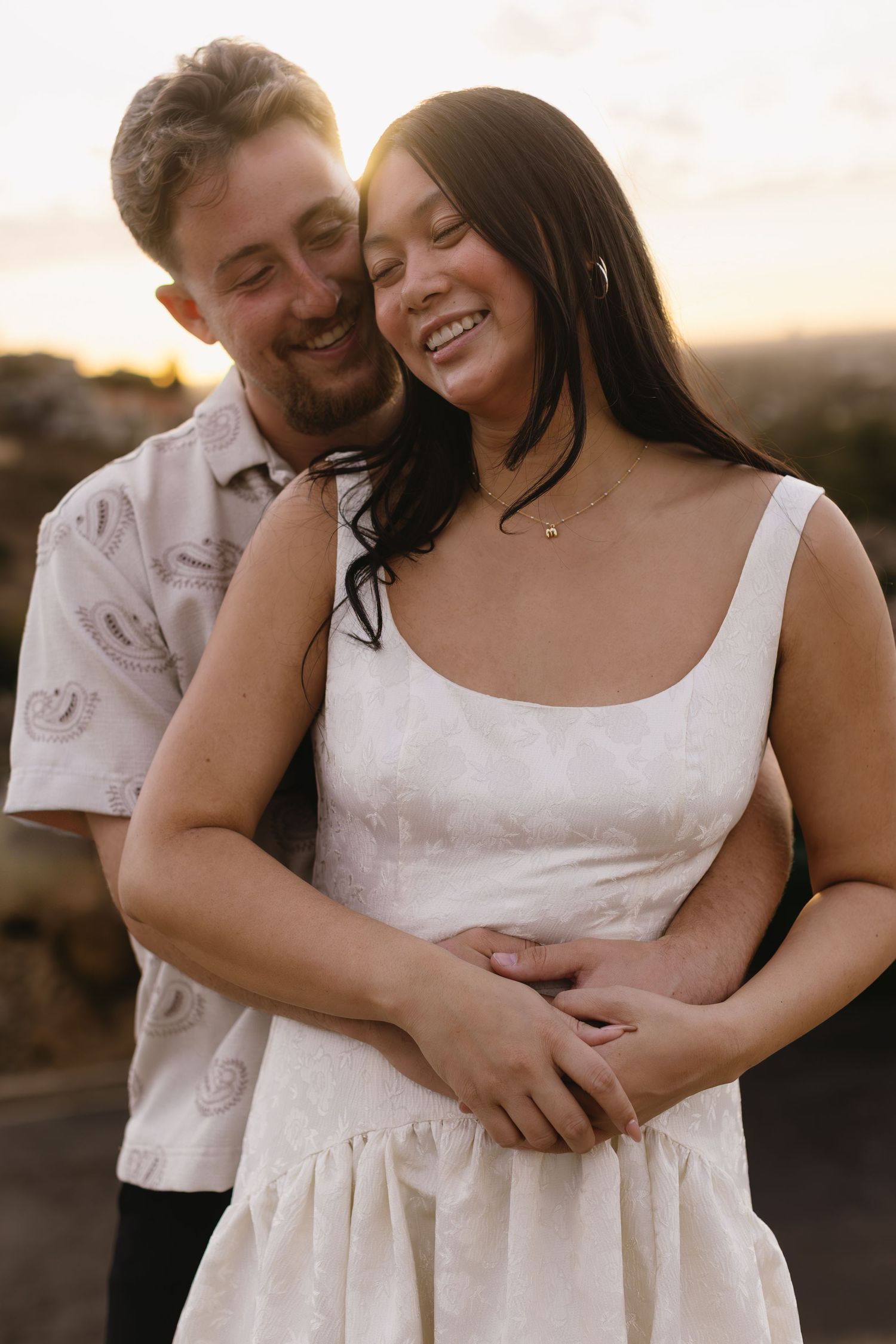 A couple embraces lovingly while standing outdoors during golden hour.