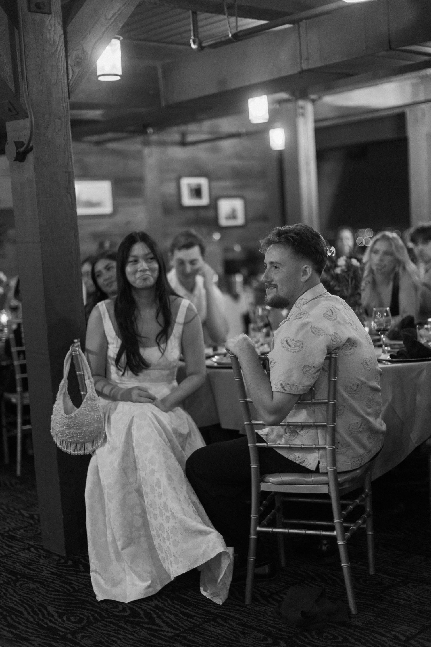 Wedding guests celebrate at tables in a rustic indoor venue with ambient lighting.
