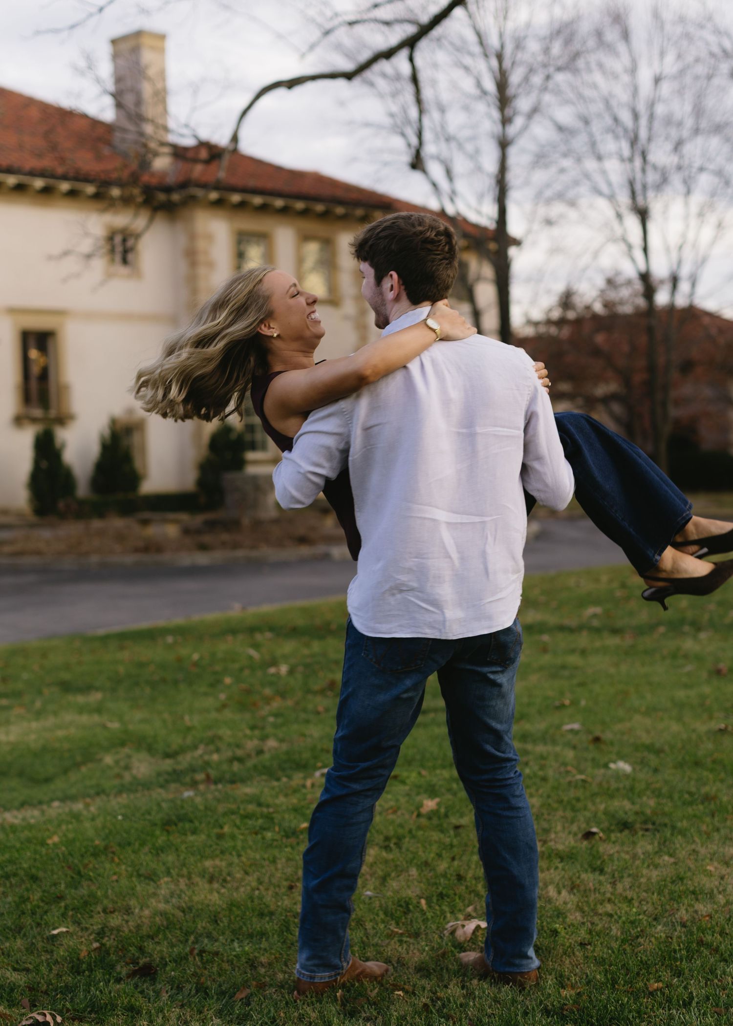 Couple spinning and dancing together on a grassy lawn near historic buildings.