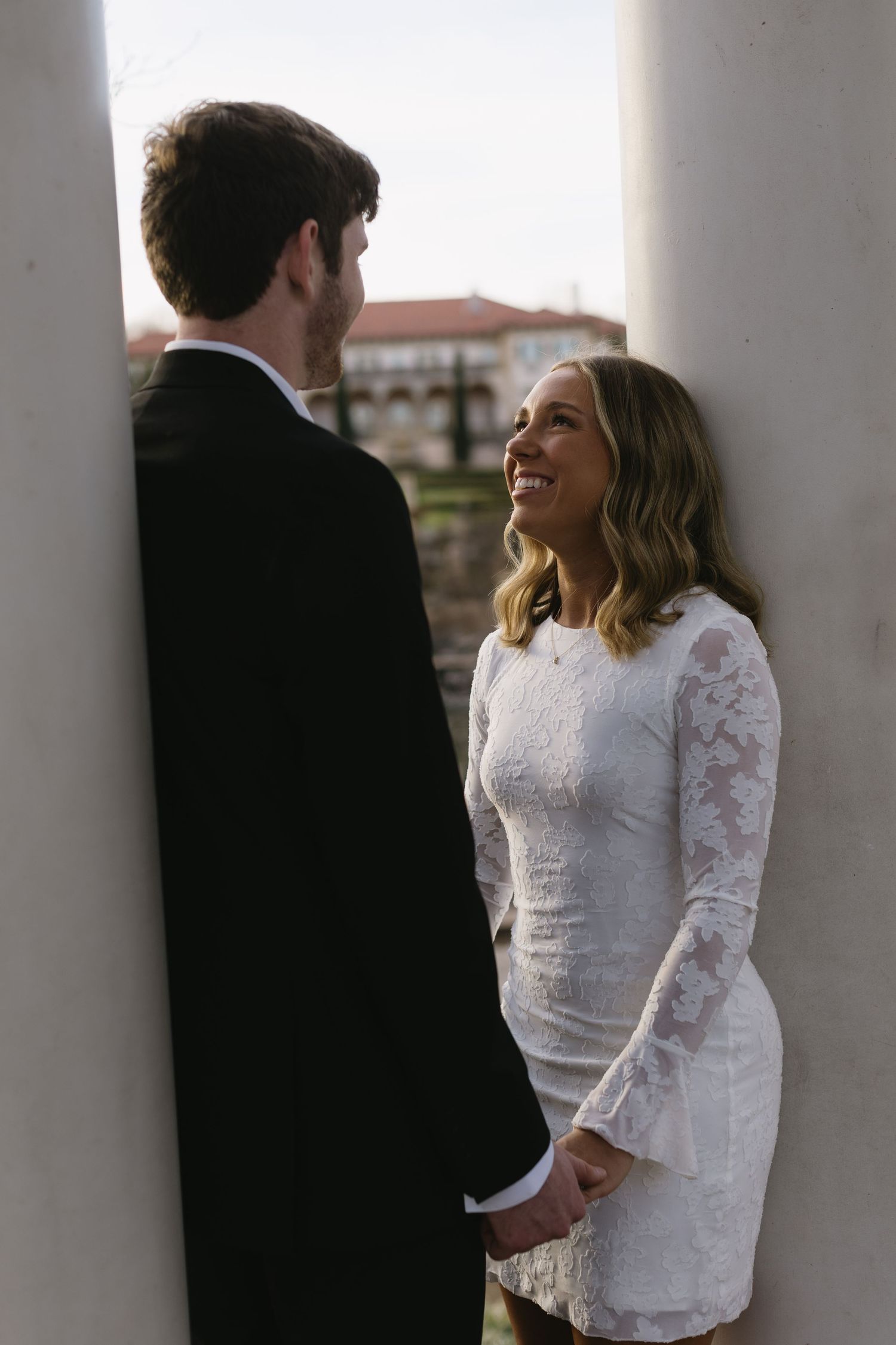 A couple sharing a joyful moment between white columns with architecture in the background.