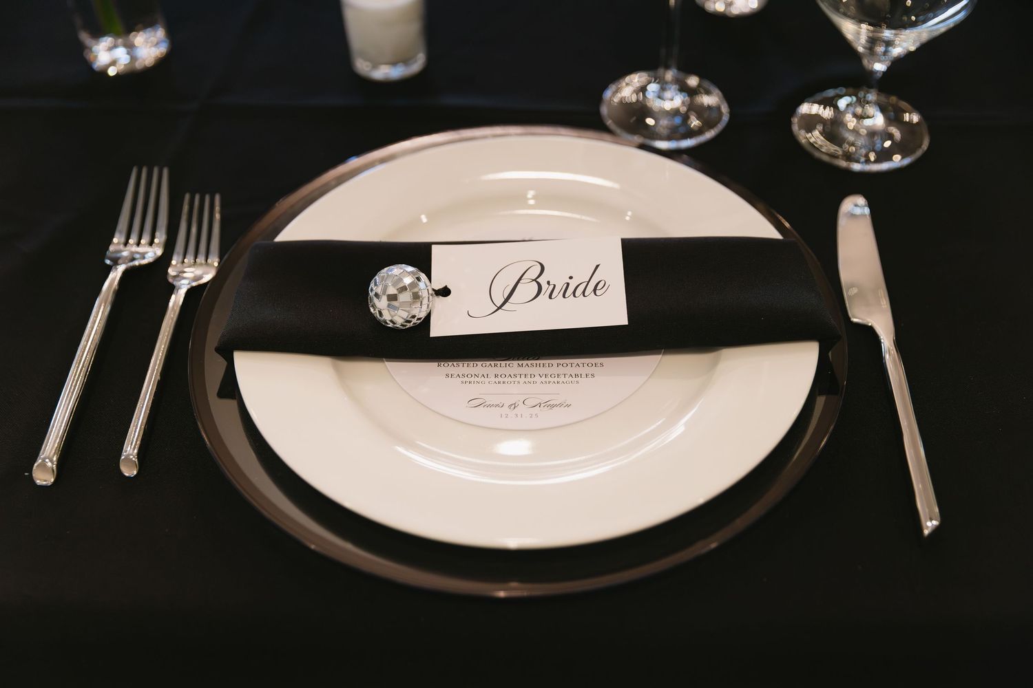 Formal place setting with white plate, silverware, and name card on black tablecloth.