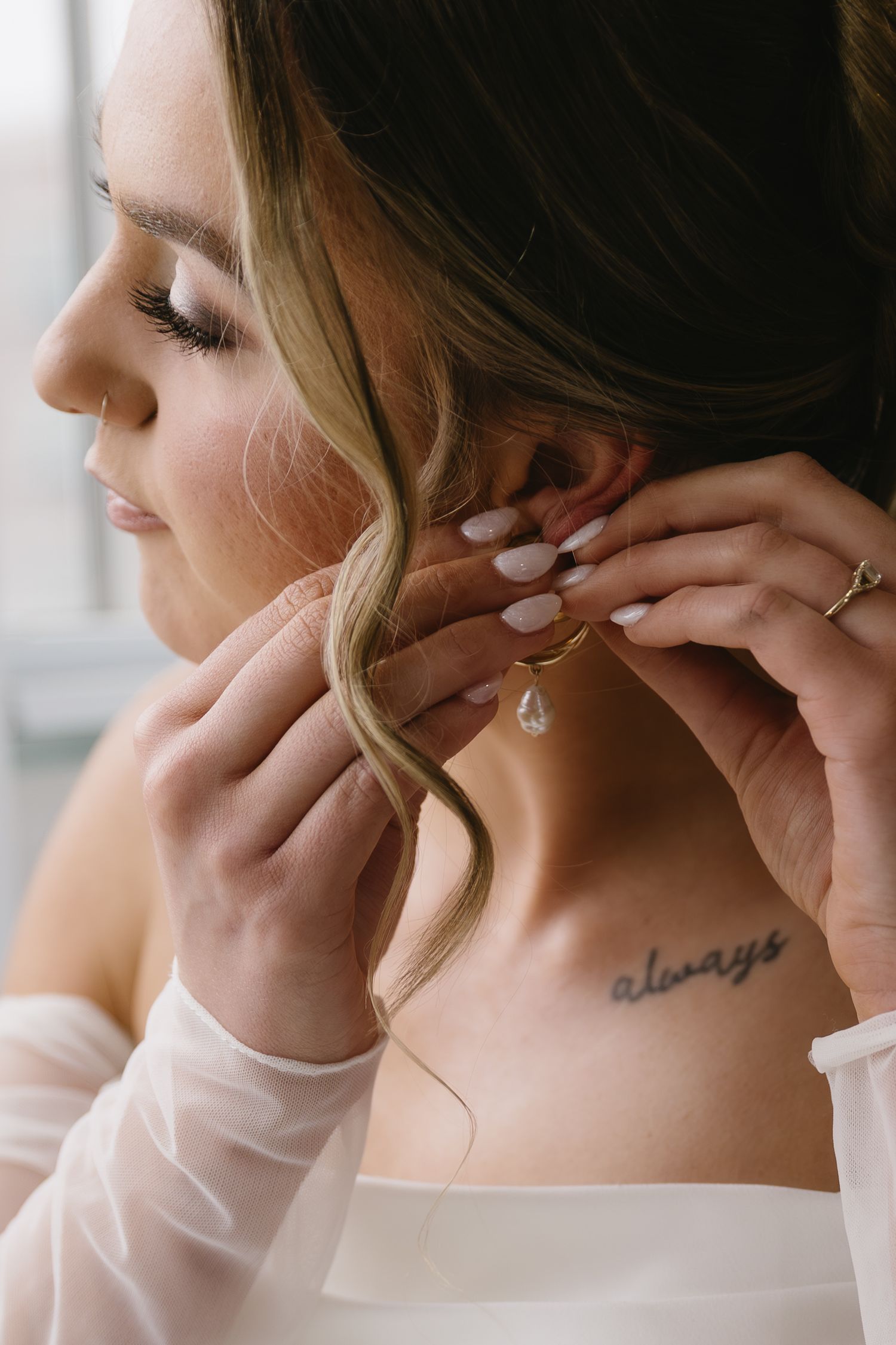 Close-up shots of someone putting on delicate earrings, showing a small 'always' tattoo on their neck.