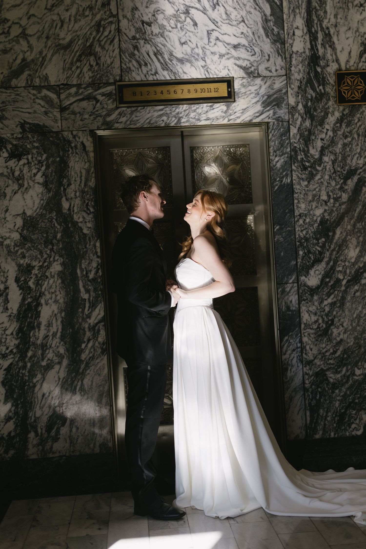 Romantic wedding couple sharing intimate moments in front of a marble wall with elevator doors.