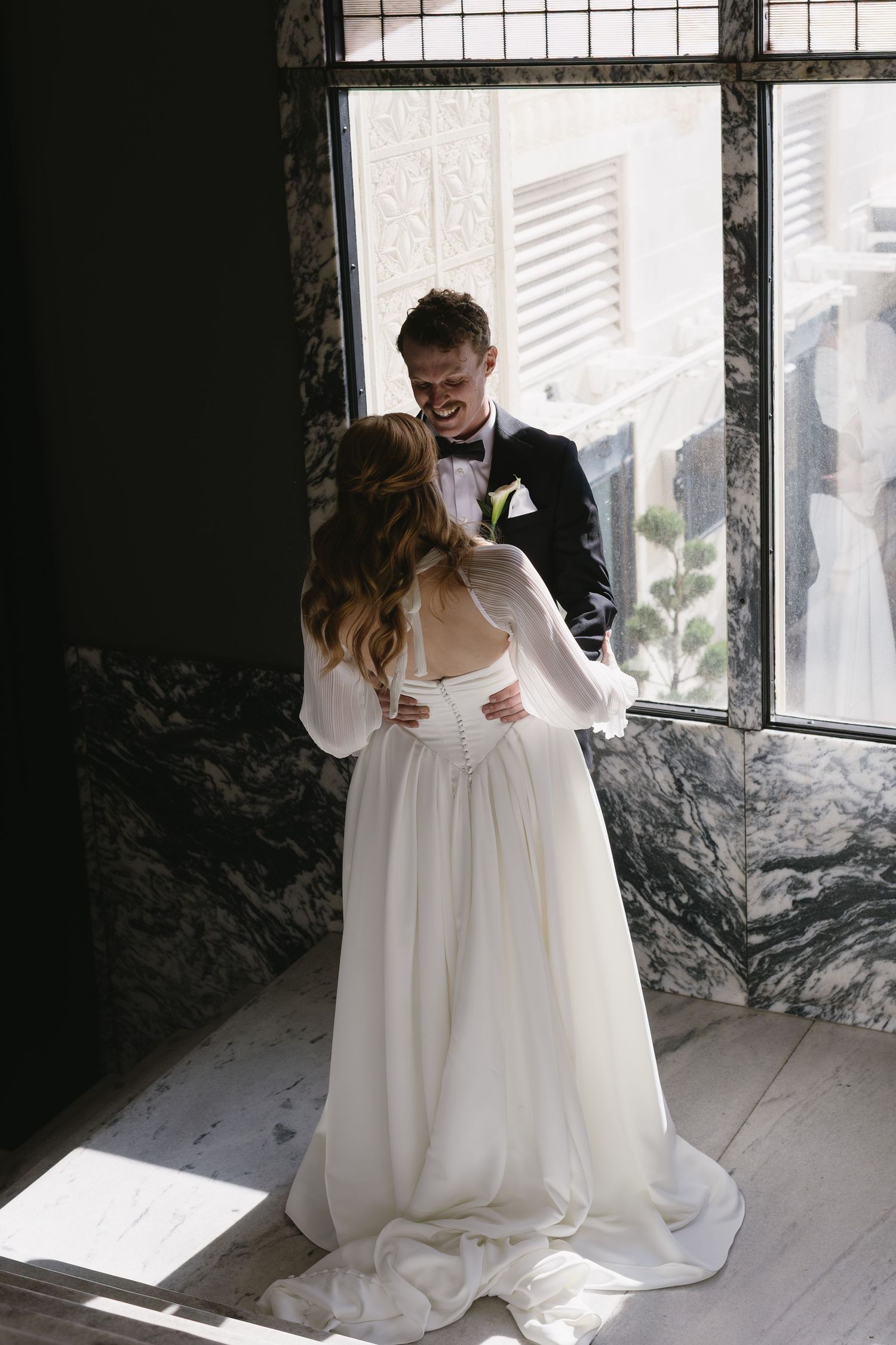 Romantic wedding moment by a sunlit window in an industrial-style space.
