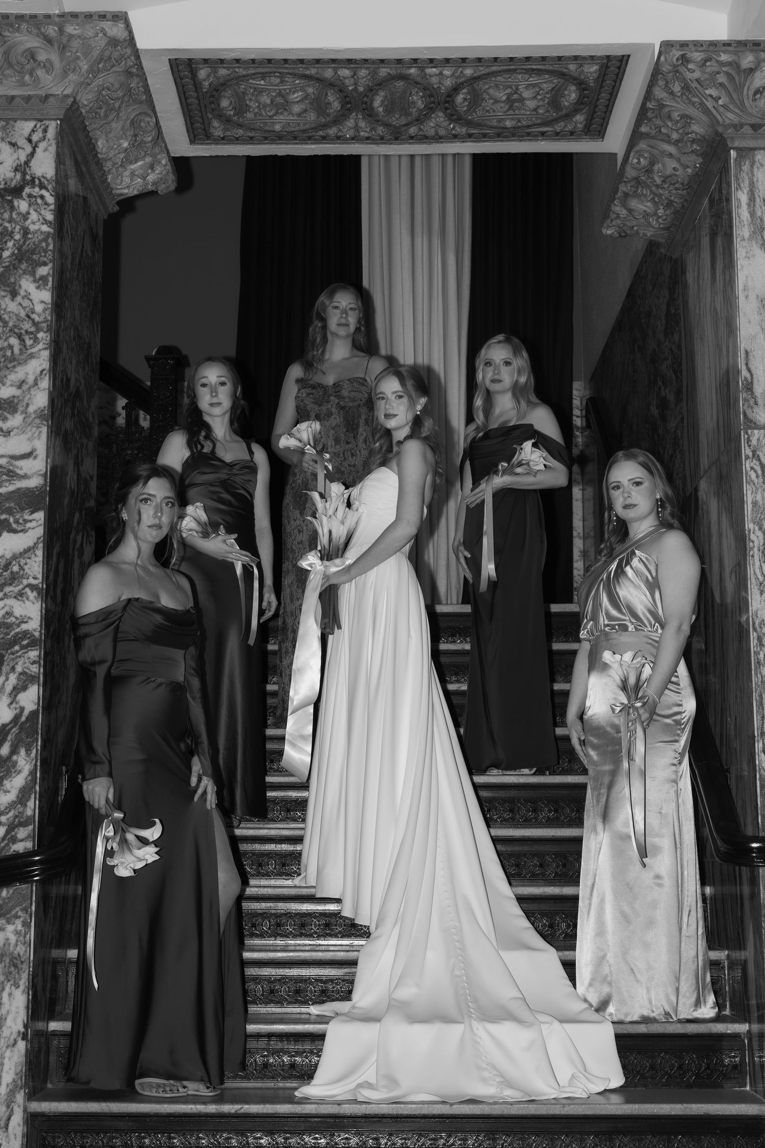 Black and white wedding party portrait on marble steps with dramatic composition.