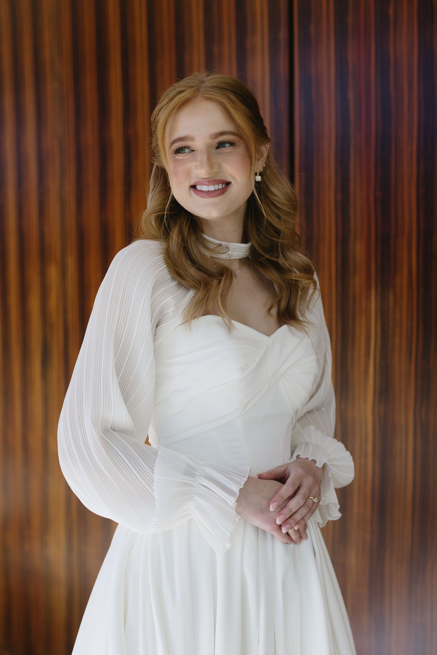 Portrait series in white dress with long sleeves against wood paneled backdrop.