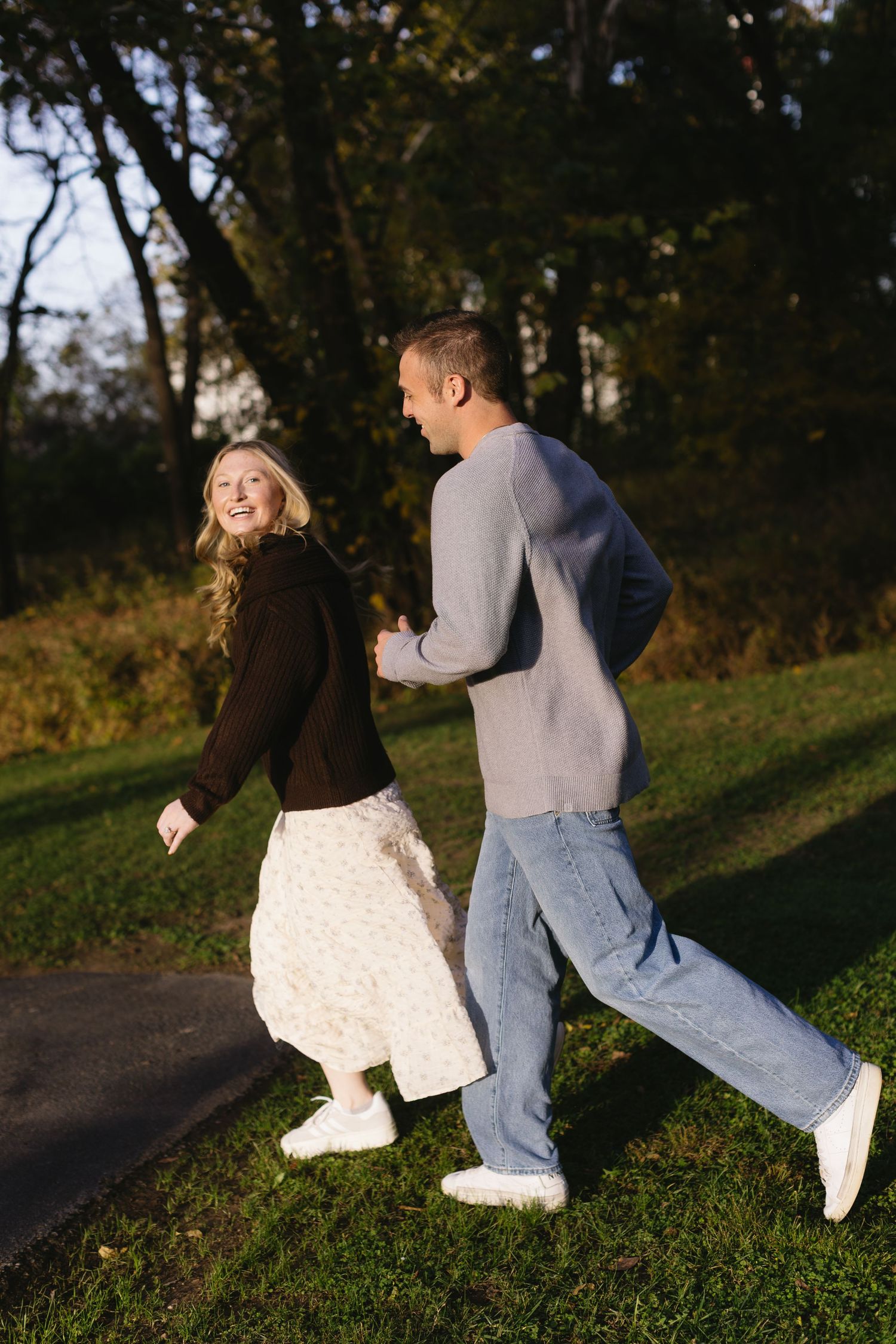 Couple dances and plays together on a grassy path during golden hour.