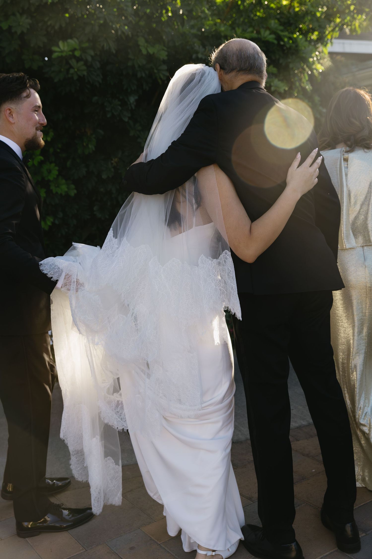 Bride in white gown dances with wedding guests at outdoor reception.