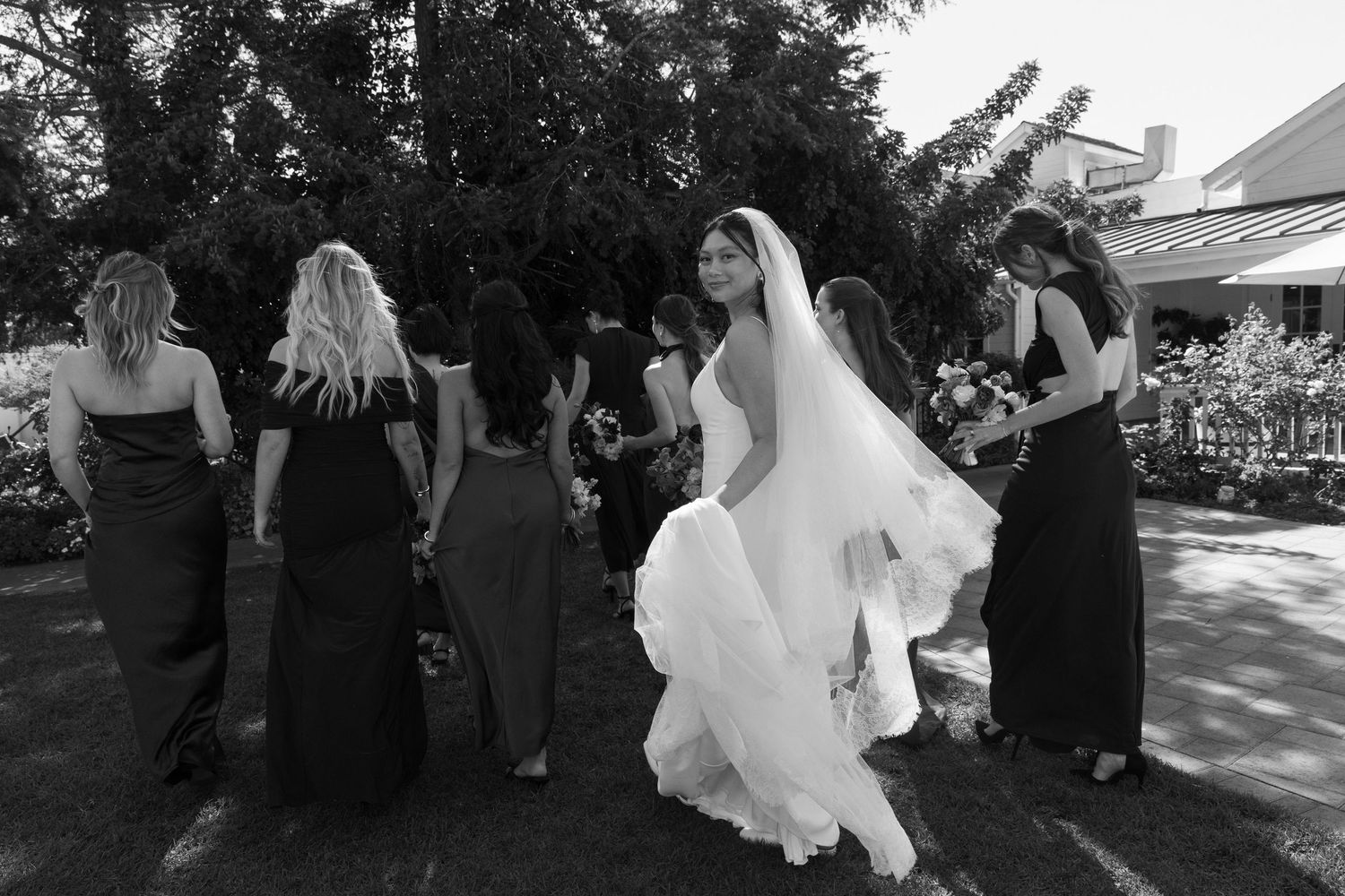 Wedding party celebrates outdoors with flowing dress movements captured in black and white.