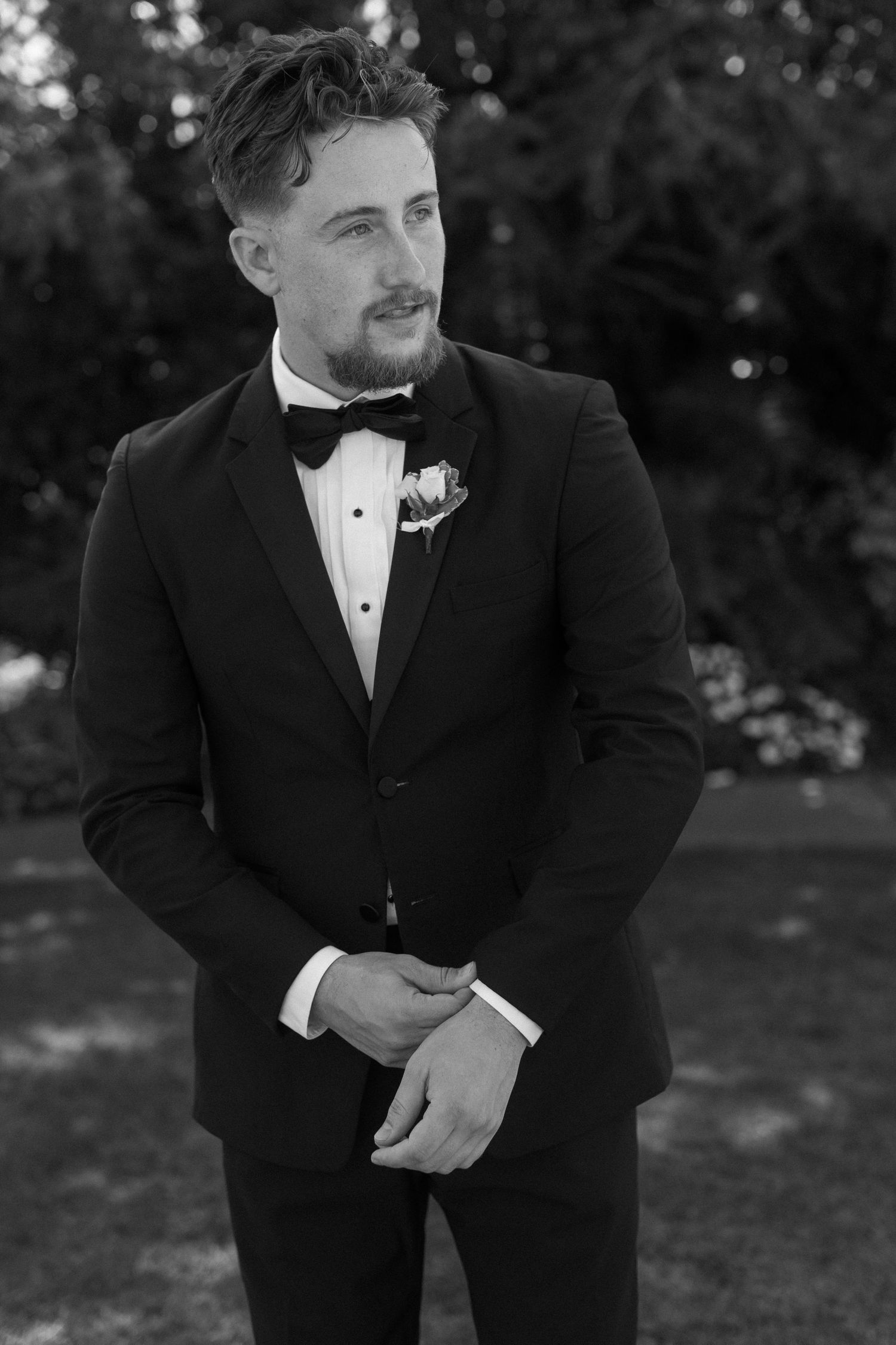 Groomsman in black tuxedo and bowtie smiling during outdoor wedding photos.