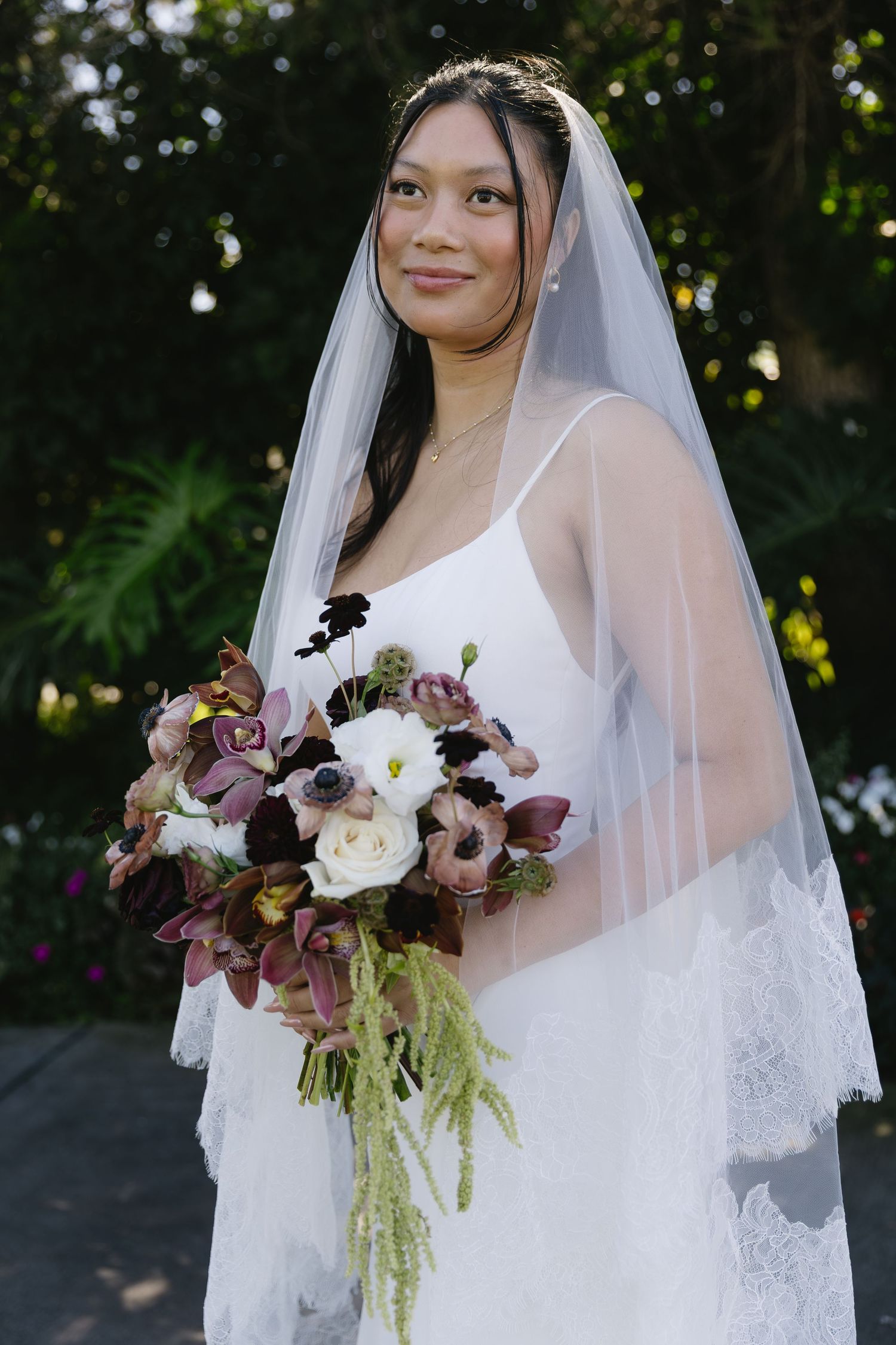 Bride holding a luxurious bouquet of white and mauve flowers with cascading greenery.
