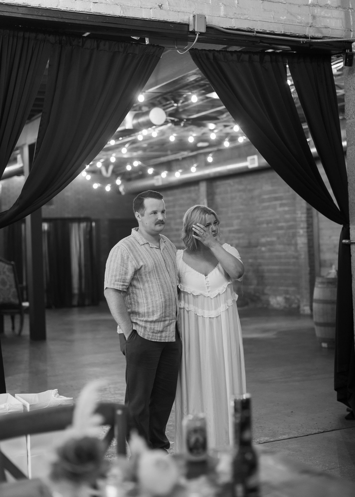 Couple dancing together in a dimly lit venue with black curtains and string lights.
