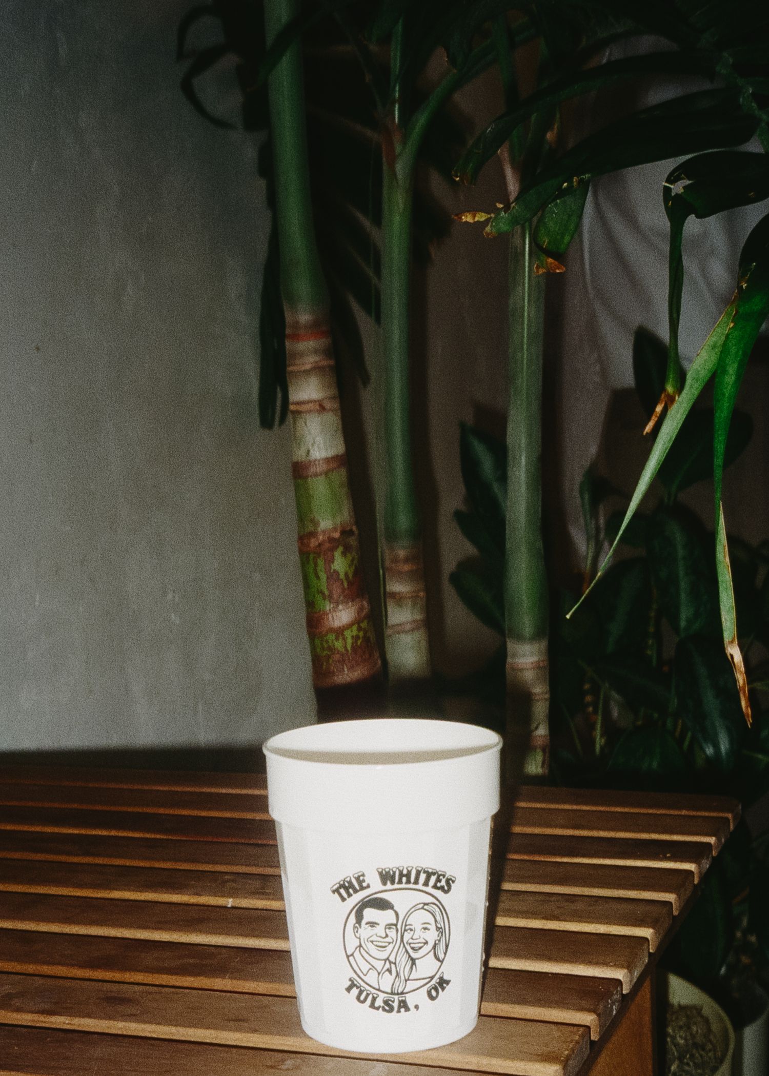 A white ceramic cup with a logo sits on wooden slats against a dark background.