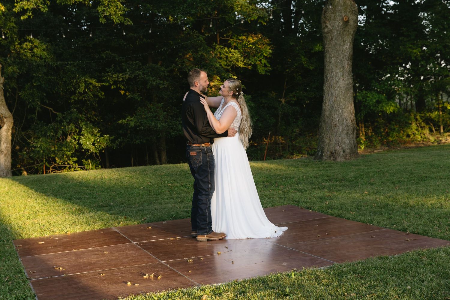 Couple sharing their first dance on a wooden platform outdoors at sunset.