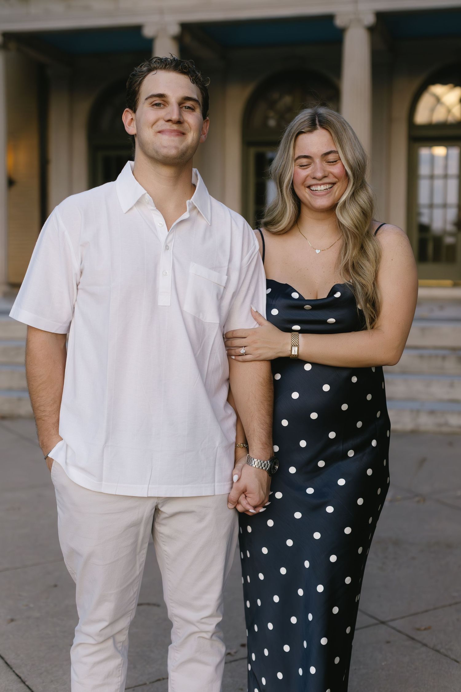 Couple poses together outdoors, wearing coordinated black polka dot dress and white outfit.