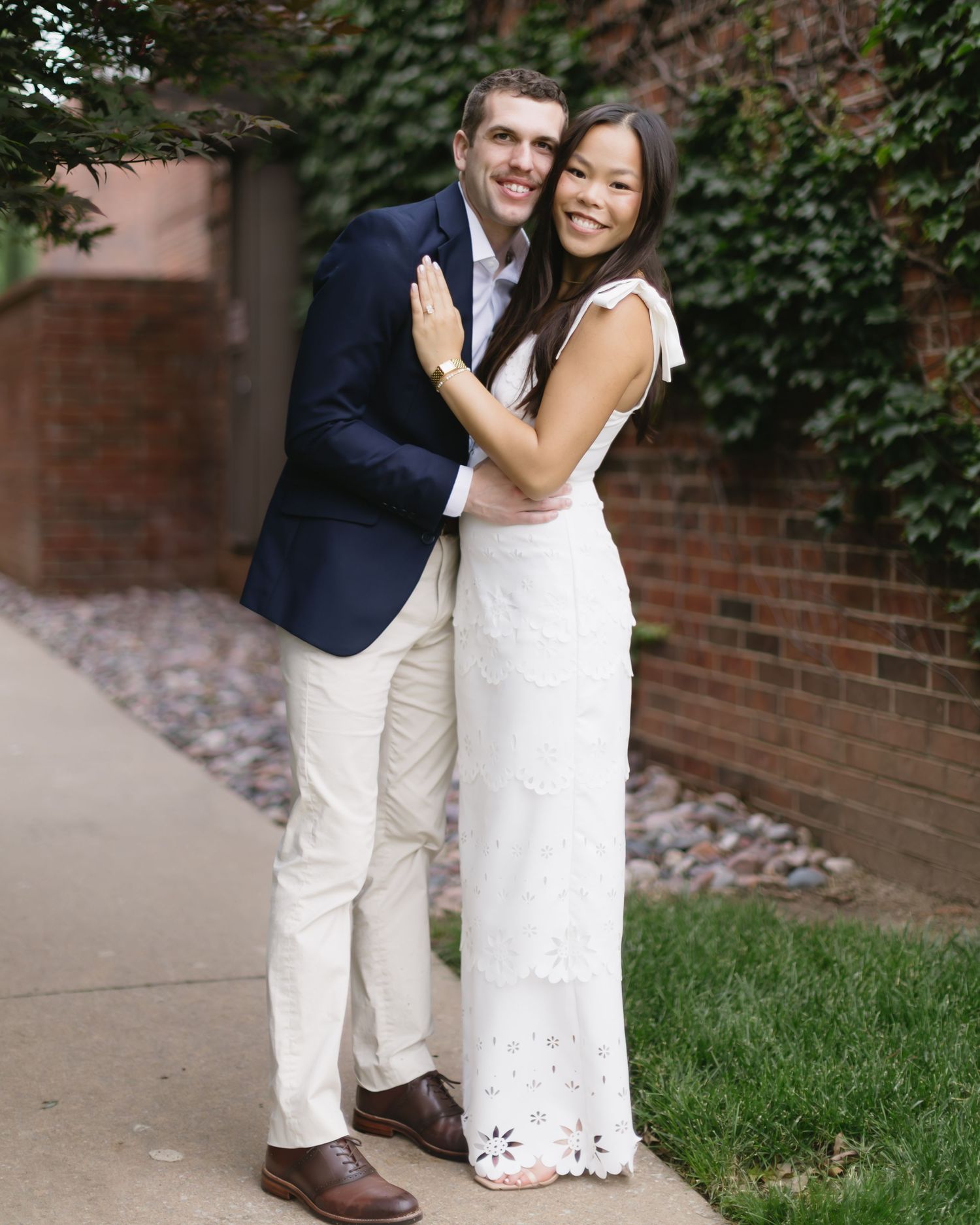 An engagement photoshoot featuring a couple in coordinated white and navy outfits against a brick wall.