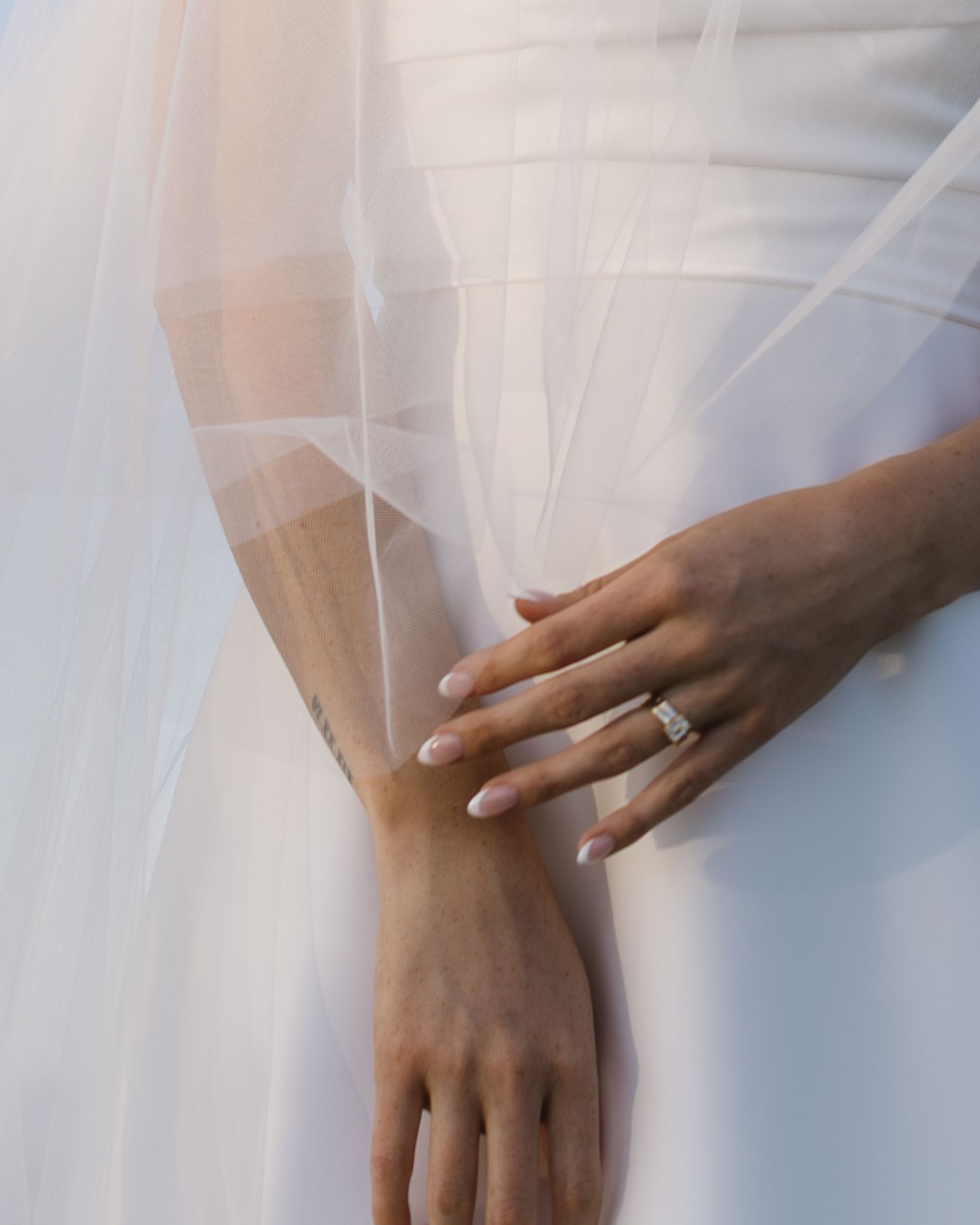 Close-up of hands wearing wedding rings with delicate white veil in soft light.