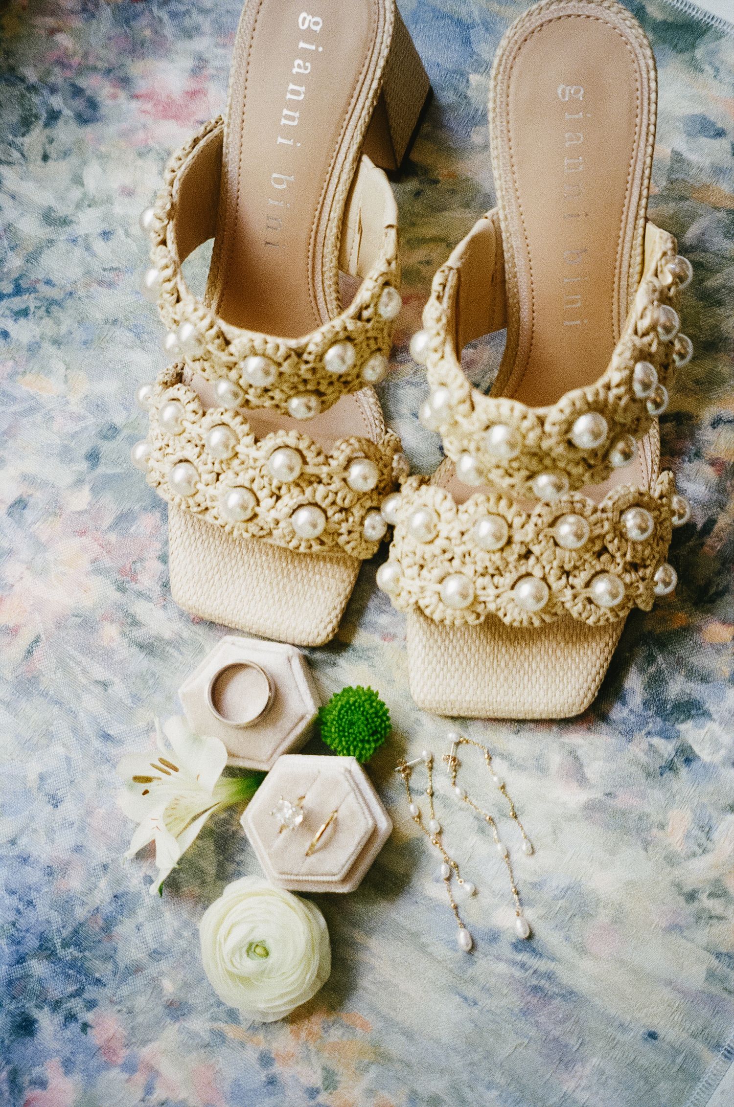 Elegant bridal shoes adorned with pearls and beaded details displayed on a textured marble surface.