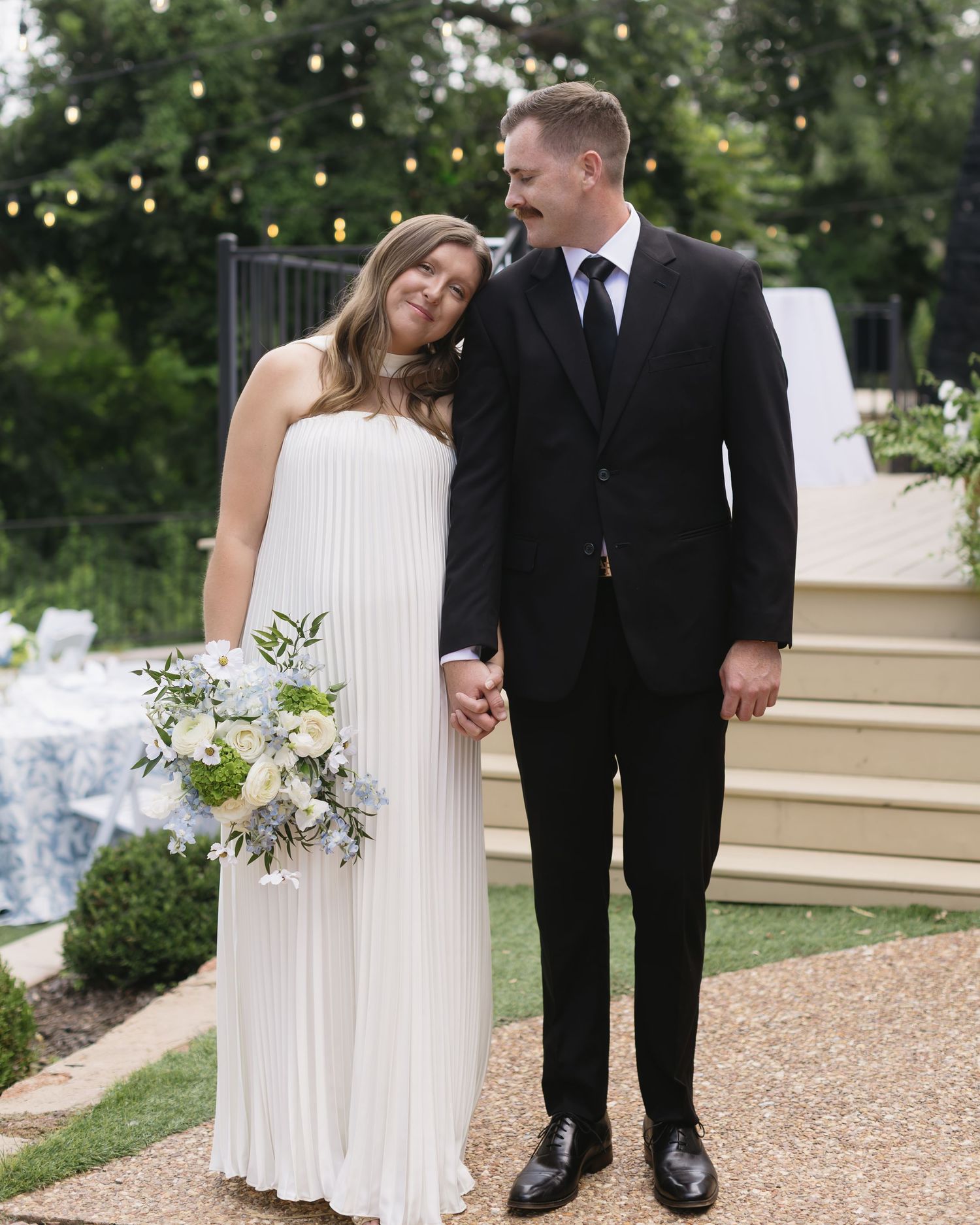 Elegant wedding couple poses together in a garden setting with a white dress and black suit.