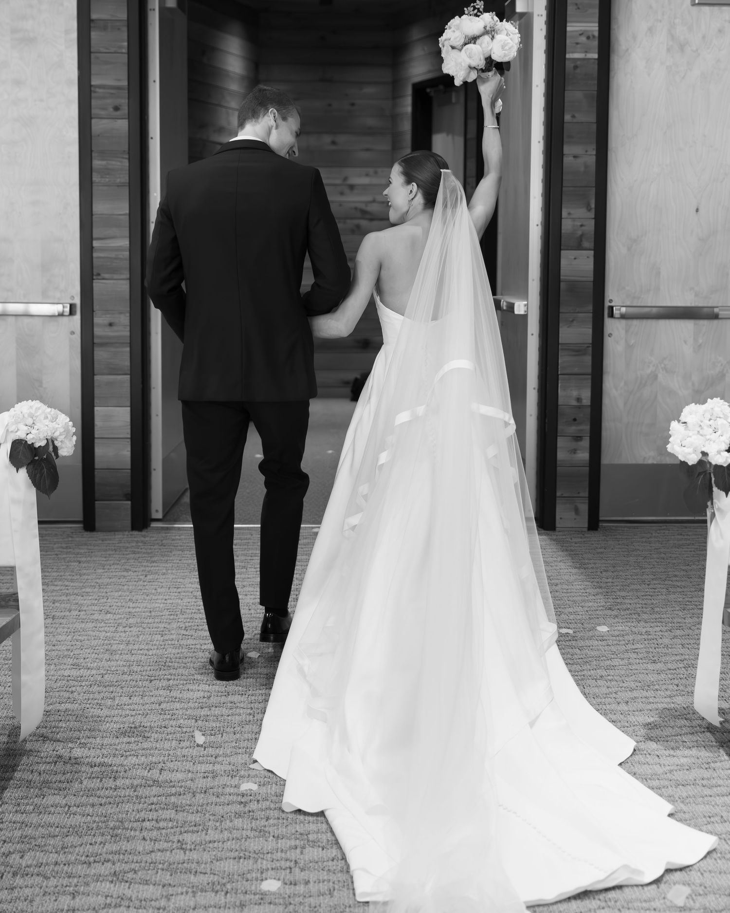 Black and white photo of newlyweds walking down a decorated hallway after their ceremony.
